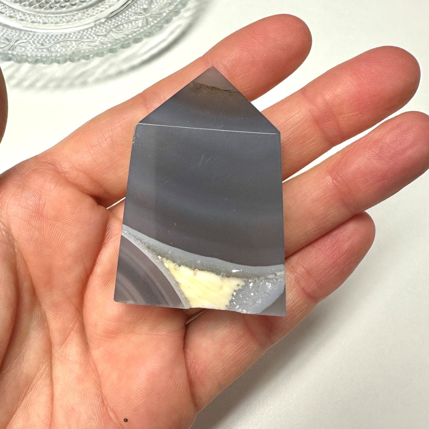 Hånd holder et Agat natur tårn, gråtonet med naturlige mønstre, på en lys baggrund.