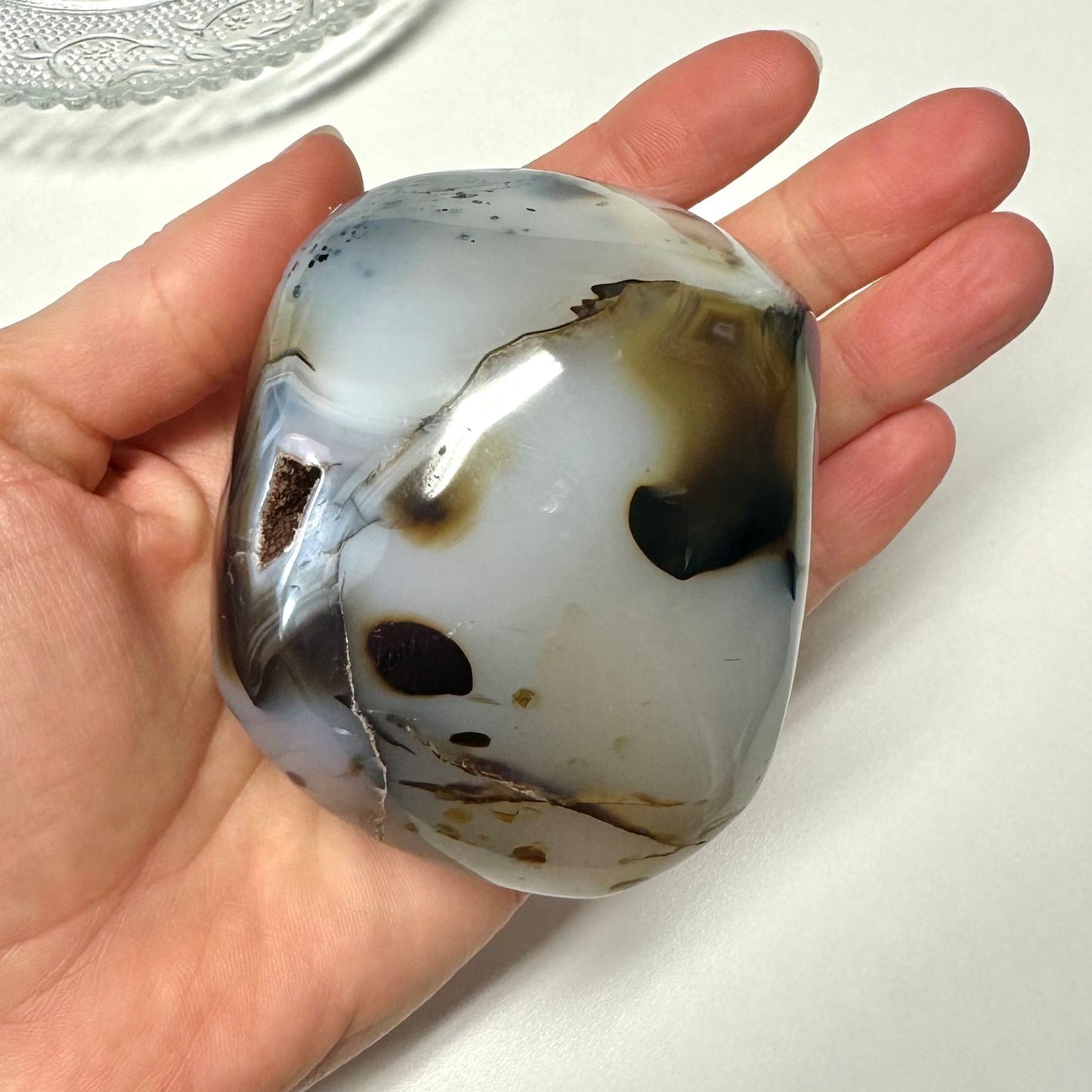 Hånden holder en Agat natur jumbo med brune og hvide mønstre, liggende på en lys baggrund.