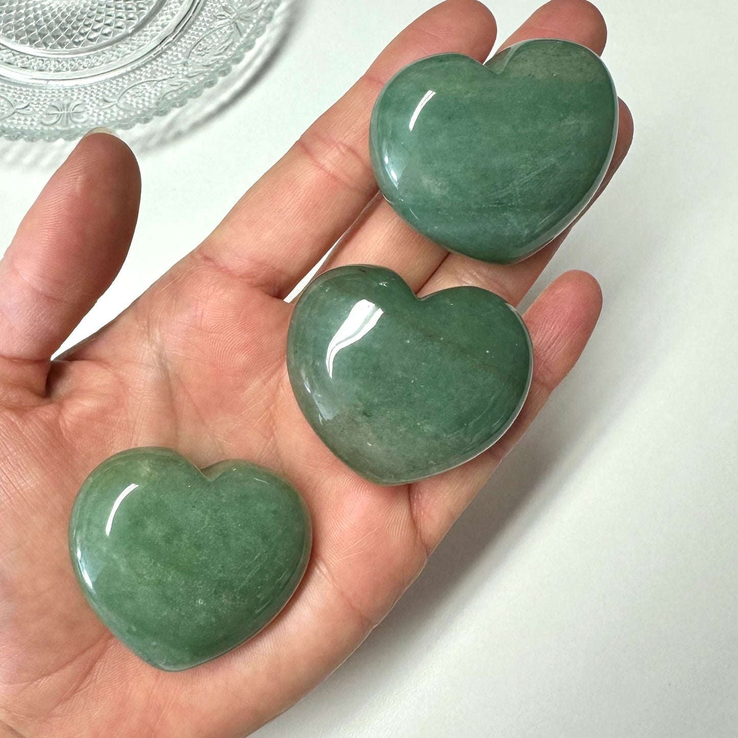 En åben hånd holder tre grønne aventurin hjerter mod en lys baggrund.