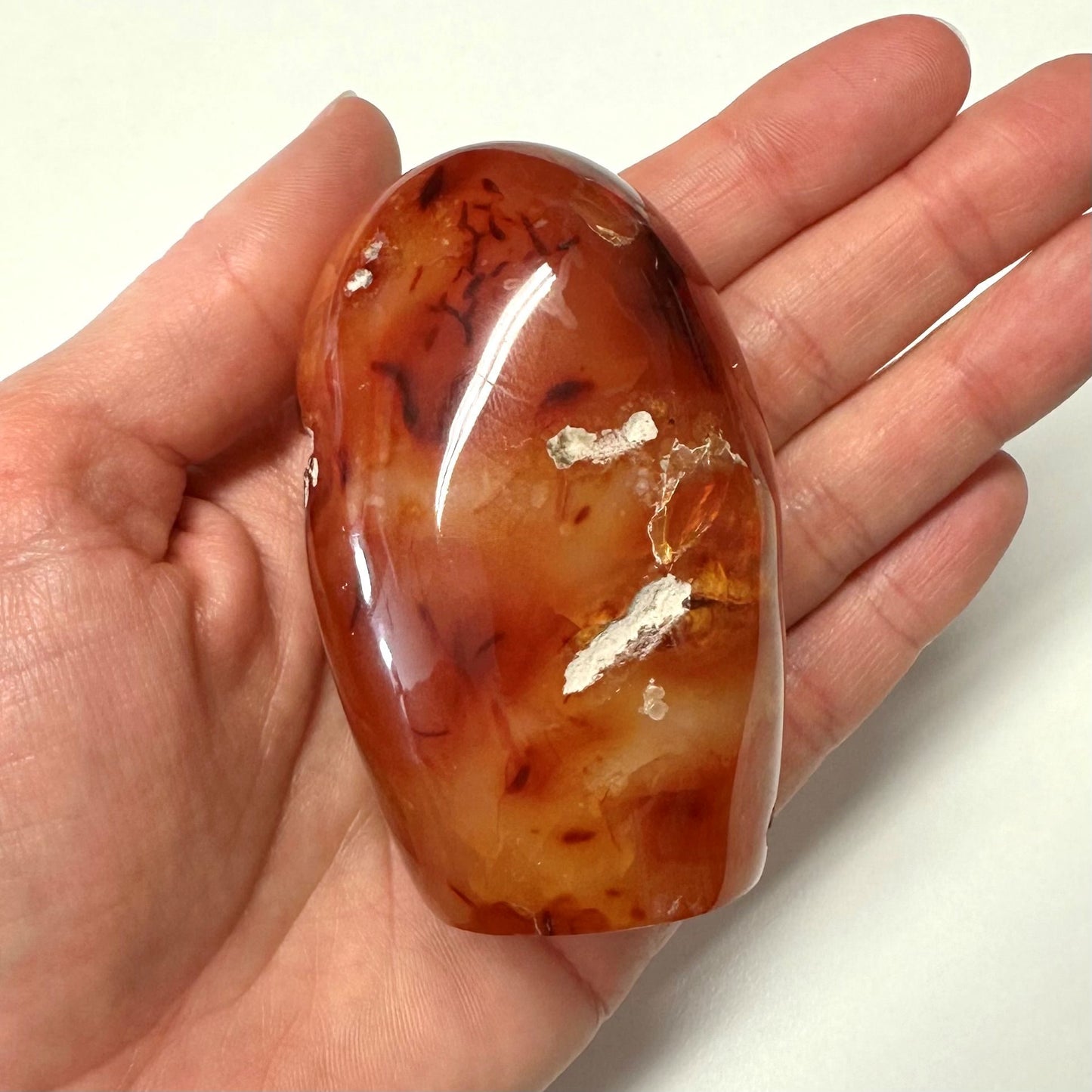 Karneol jumbo-sten med glat overflade og mønstre holdt i en hånd, der viser dens størrelse og farvevariationer.
