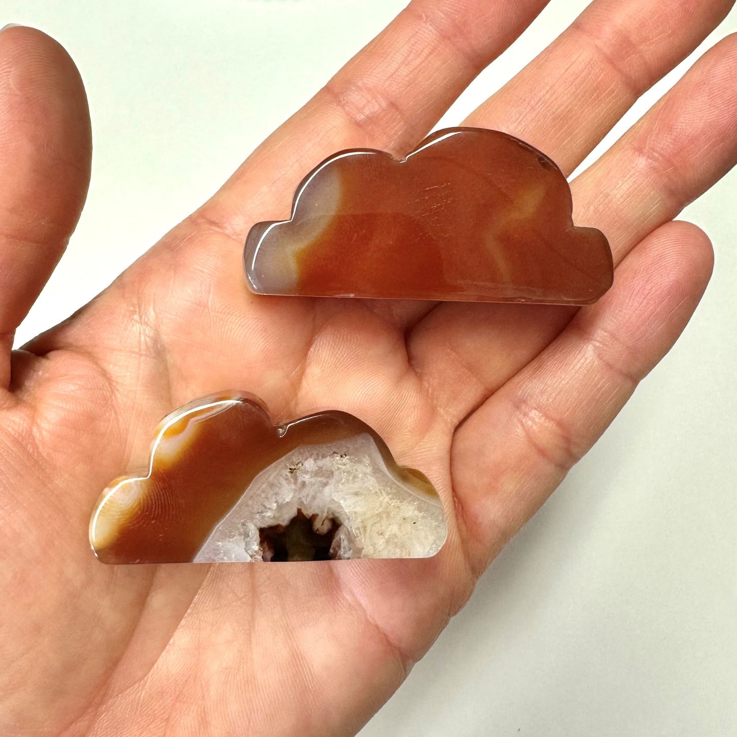 To karneol stenformede skyer i en hånd. En har en hvid geode indeni.