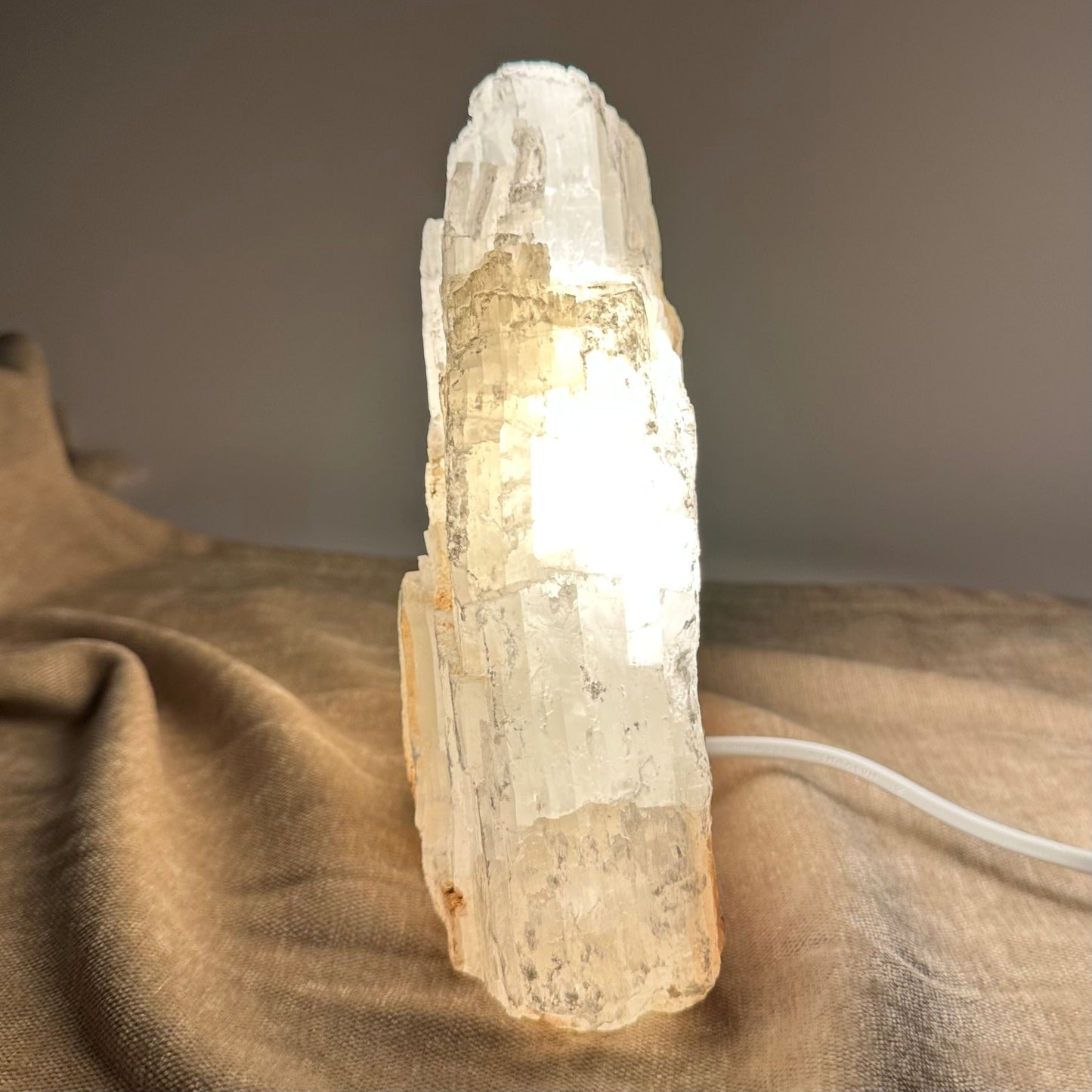 Mexicansk Selenit lampe nr 1, oplyst og placeret på en beige overflade.