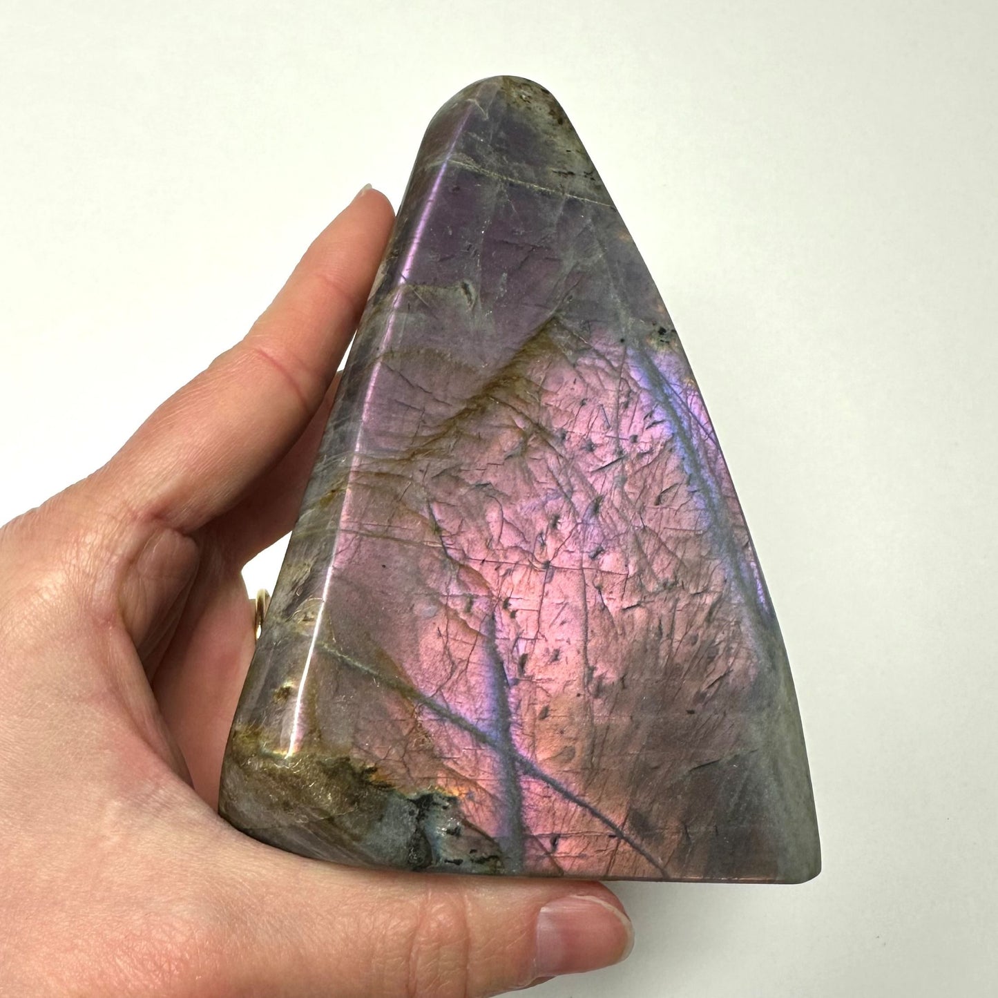 Labradorit i freeform, holdt i hånden, med en smuk solnedgangsglans i lilla og pink nuancer.