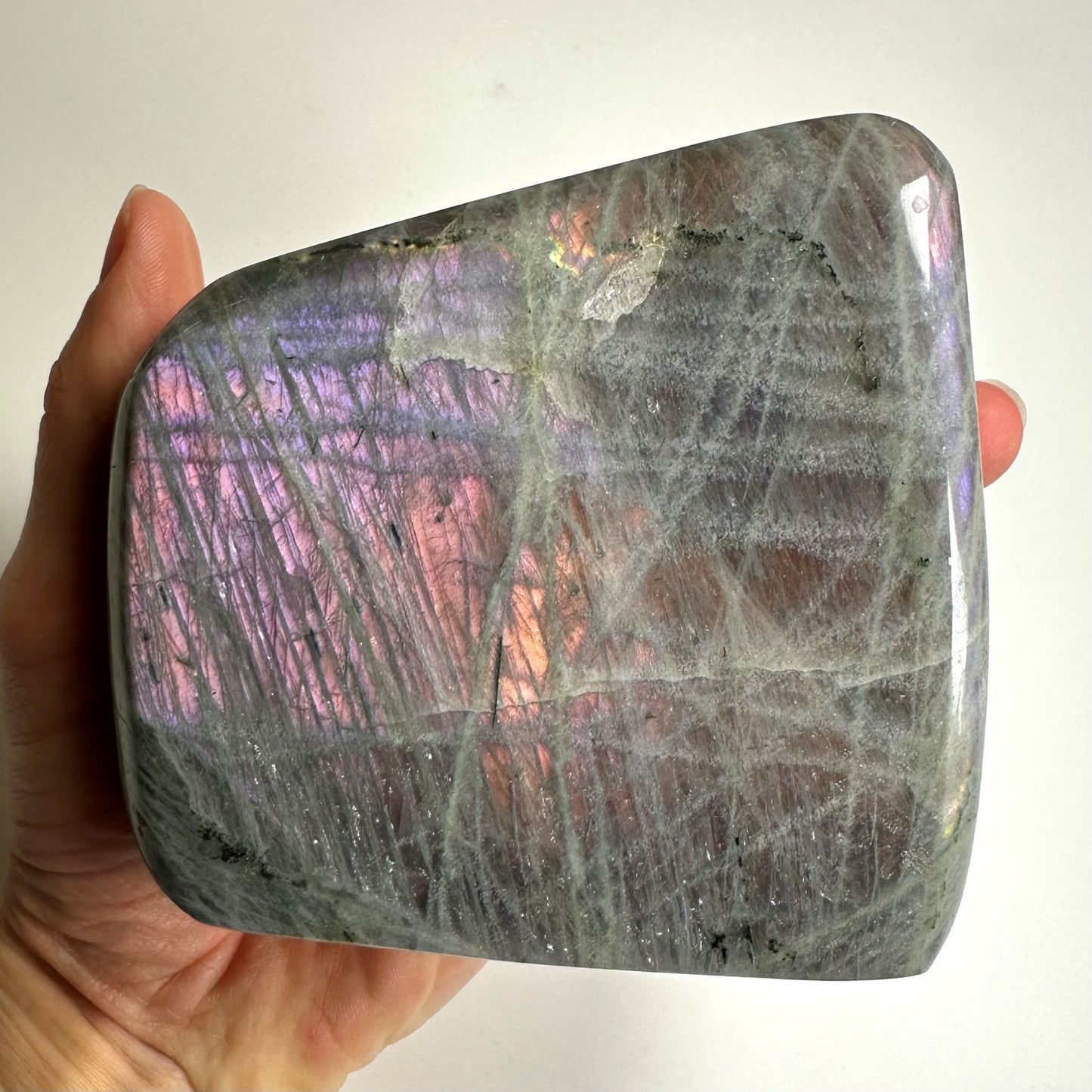 Labradorit i fri form med farver, der minder om en solnedgang, holdt i en hånd.