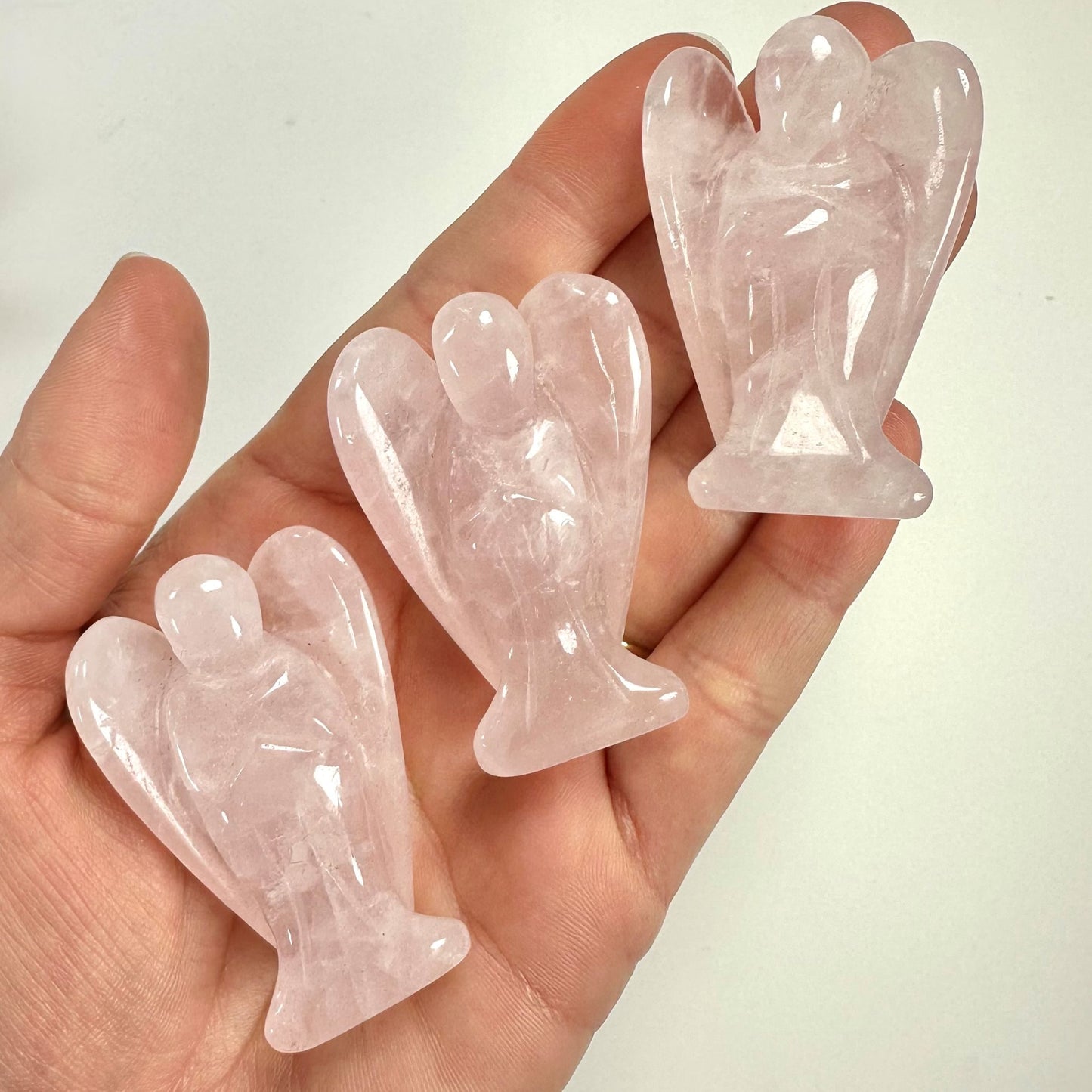 Tre små Rosenkvarts engle holdes i en hånd, skåret i lyserød sten med gennemsigtigt udseende.
