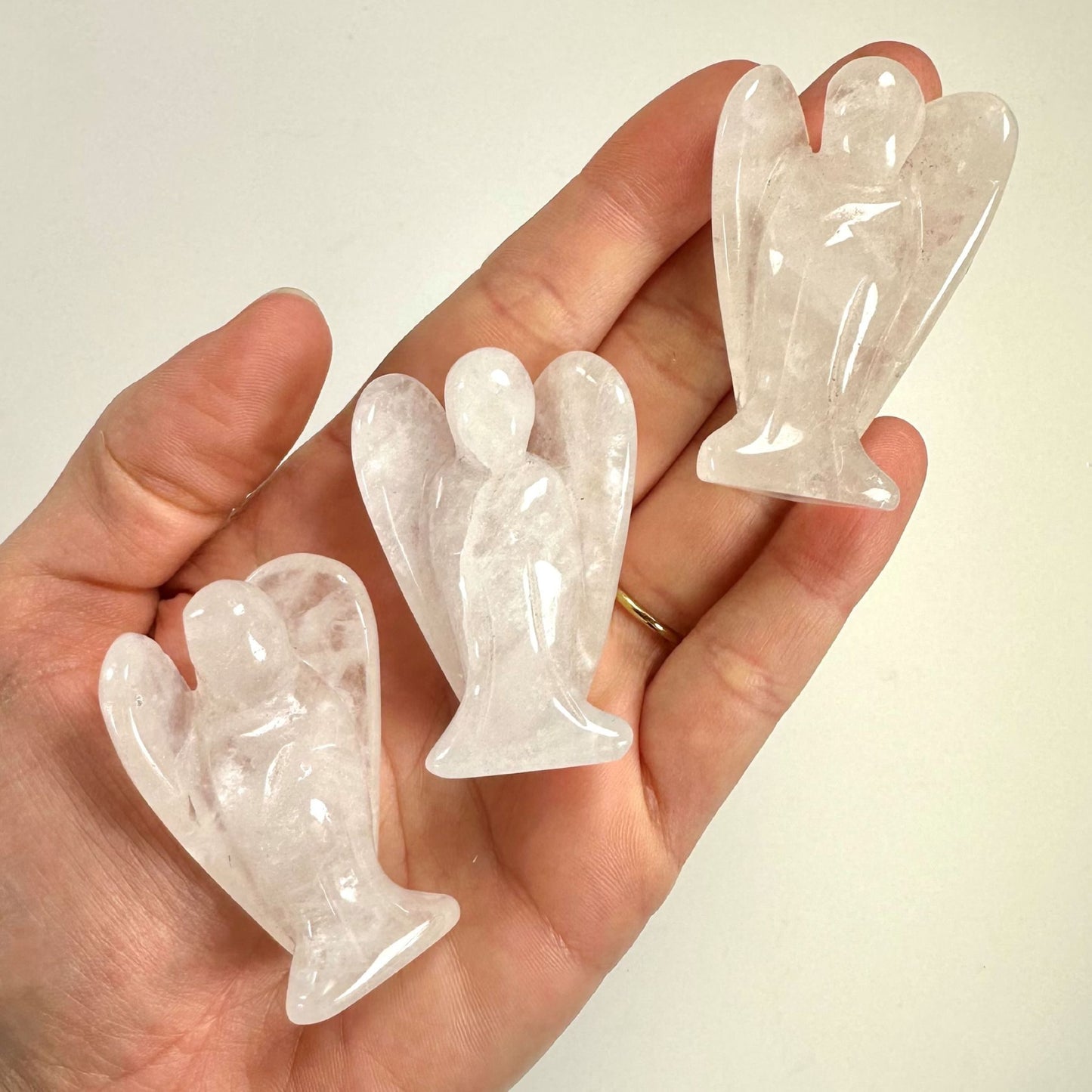 Hånd holder tre udskårne bjergkrystal engle på en lys baggrund.