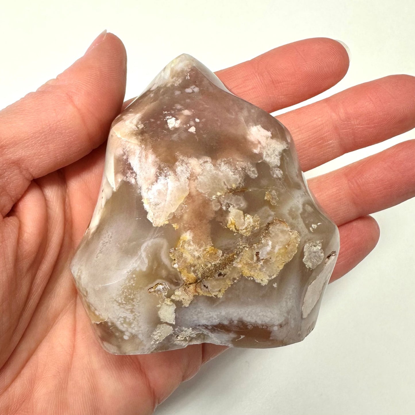 Hånd holder en blomster agat flamme i nuancer af brun og beige med hvide mønstre.