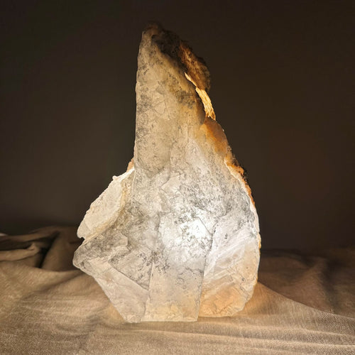 Mexicansk Selenit lampe nr 19: Naturlig formet sten med varm glød, placeret på en tekstureret overflade.