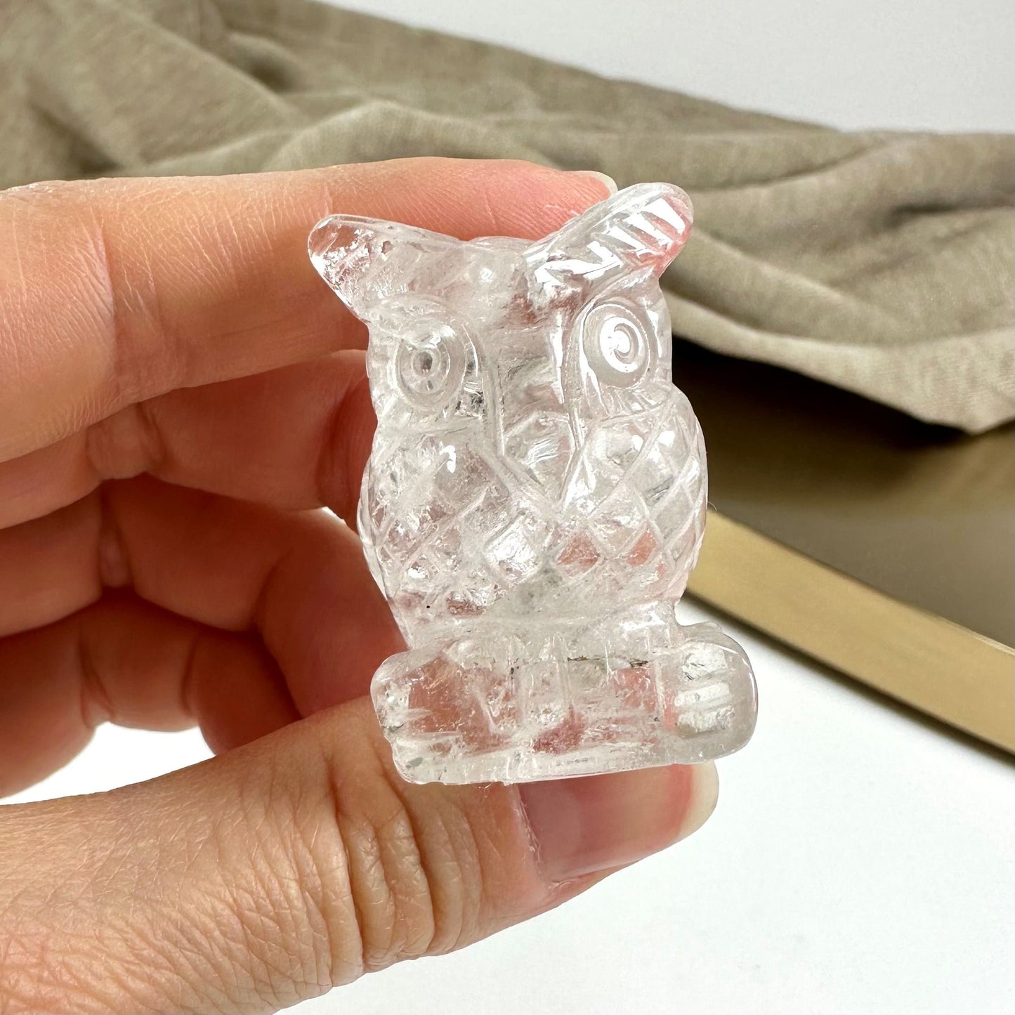 Hånd holder en lille bjergkrystal uglefigur mod en lys baggrund.