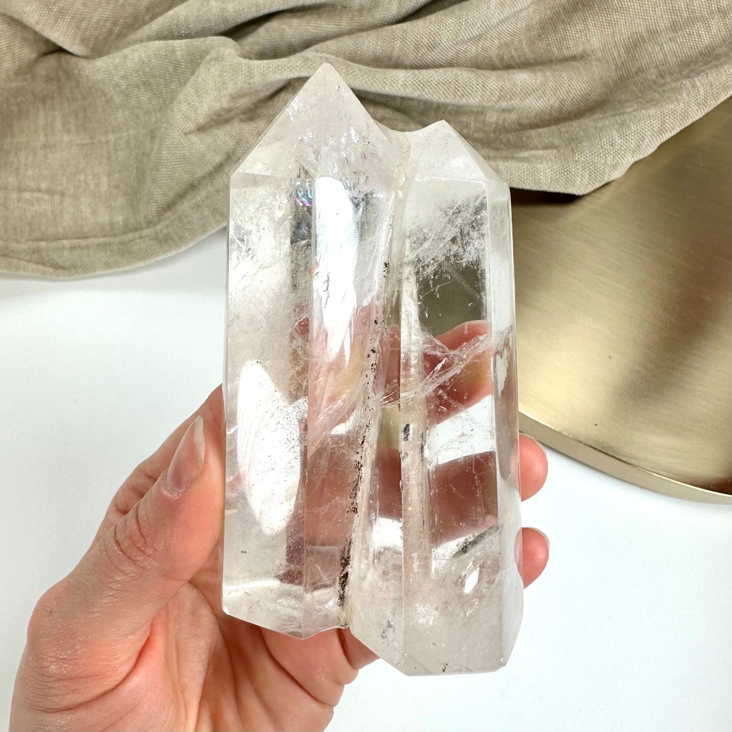 Hånd holder et klart bjergkrystal tårn mod en lys baggrund med stof og en rund bakke.