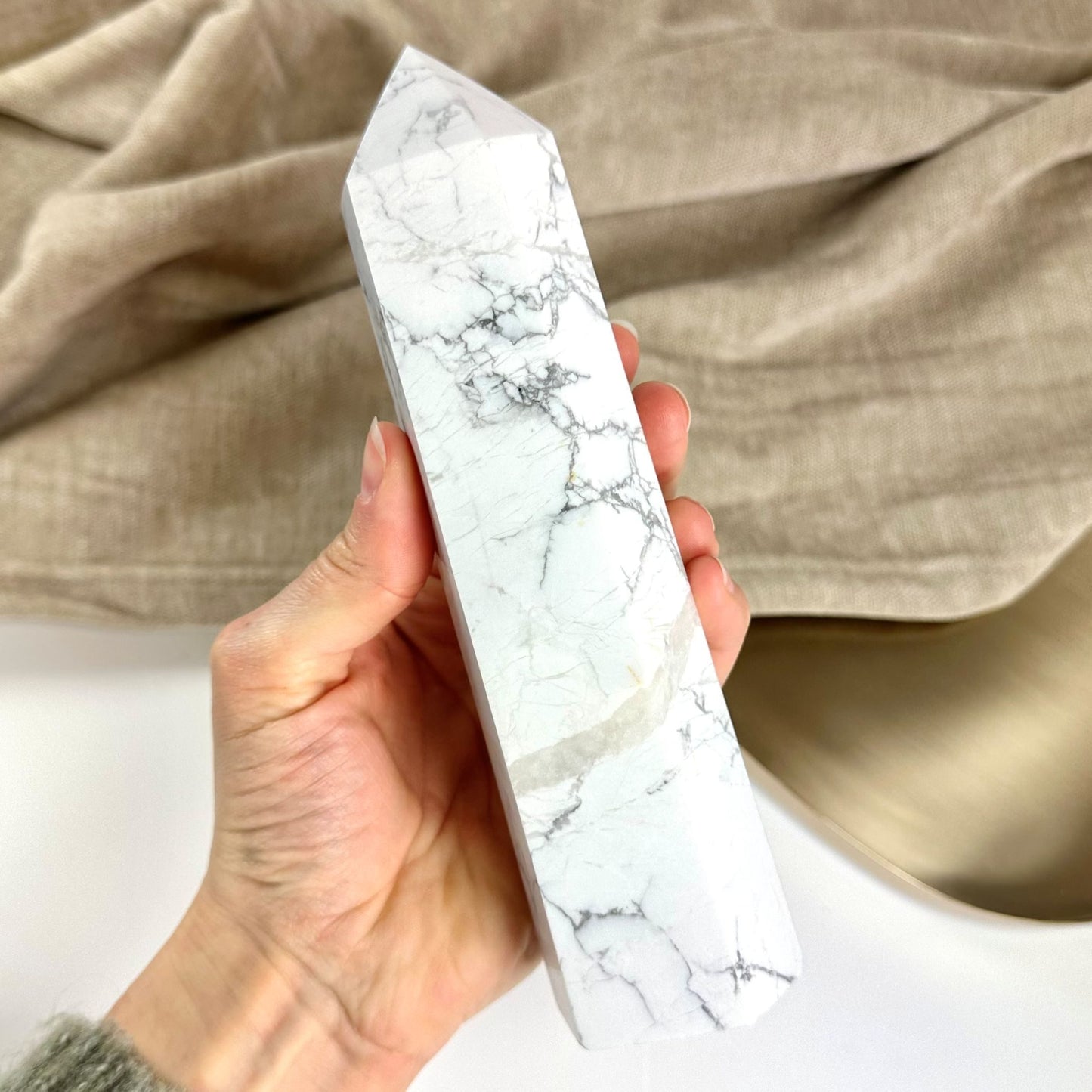 Håndholder et hvid howlit tårn mod en beige baggrund.