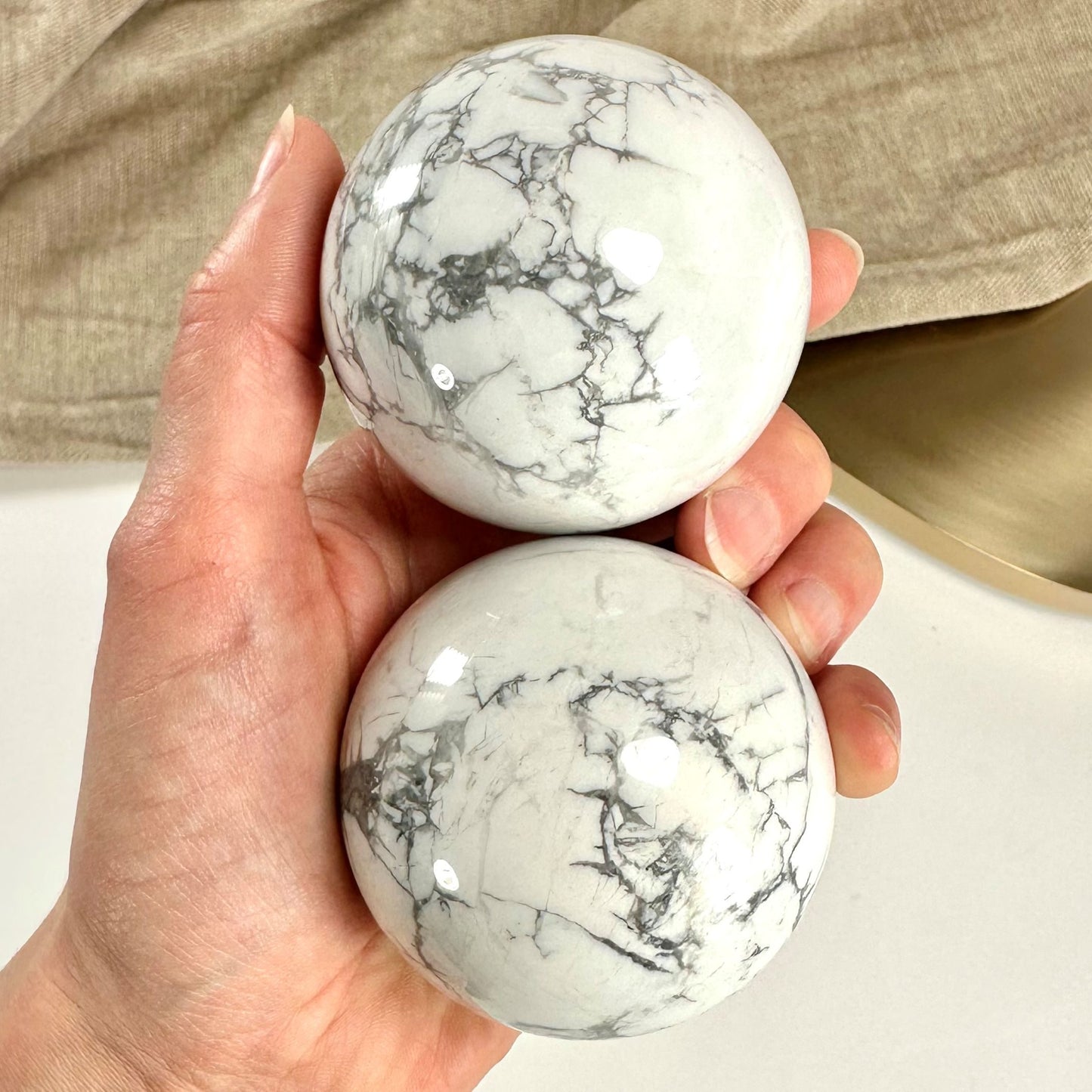 En hånd holder to hvide howlit kugler med grå marmorering mod en lys baggrund.