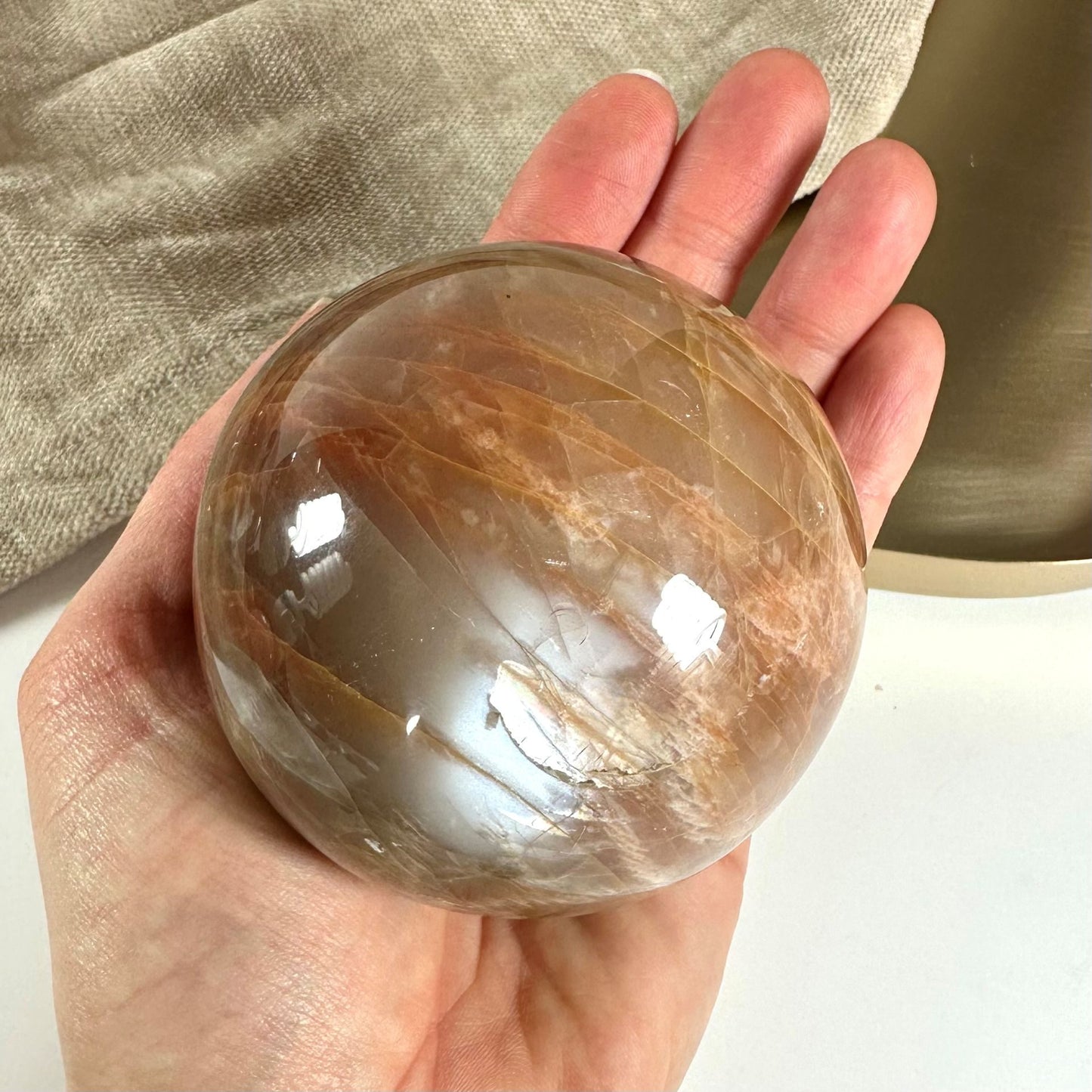 En hånd holder en glat og skinnende fersken månesten kugle mod en neutral baggrund.