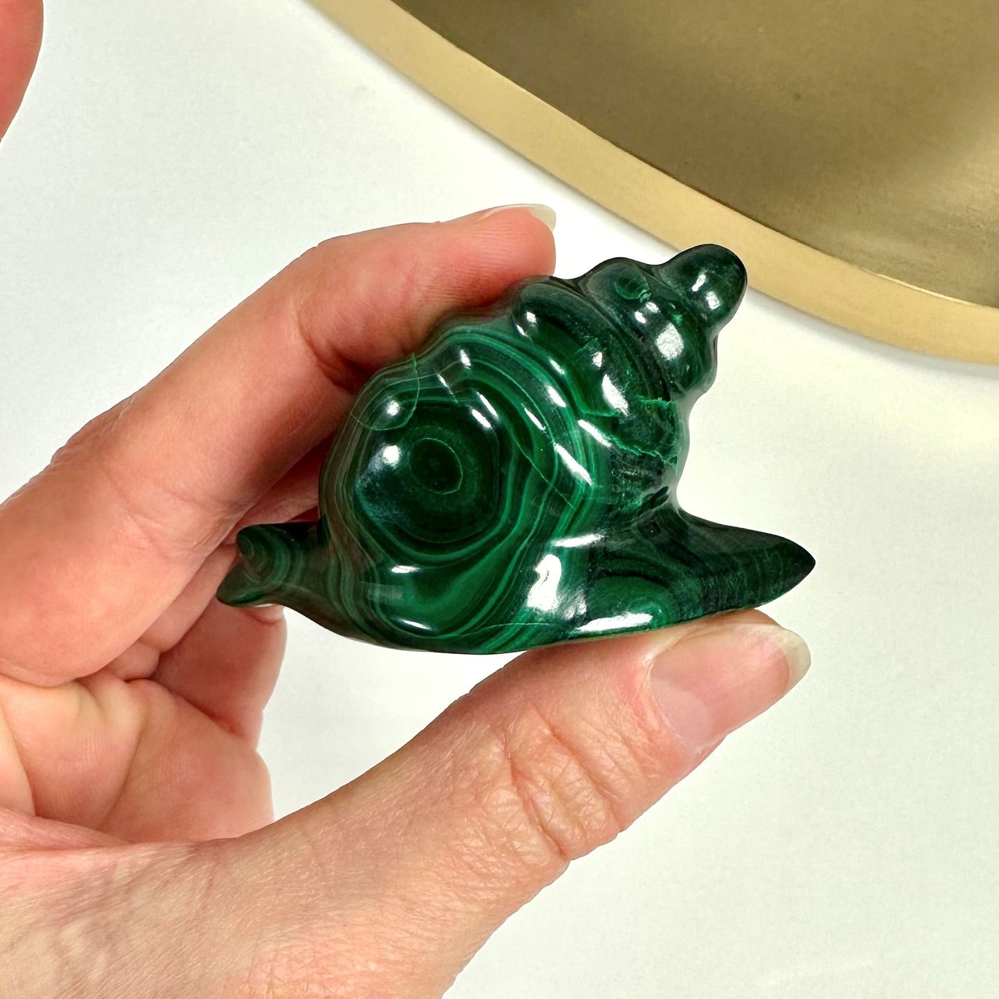 Hånd holder en Malakit snegl lavet af grøn malakitsten mod en lys baggrund.