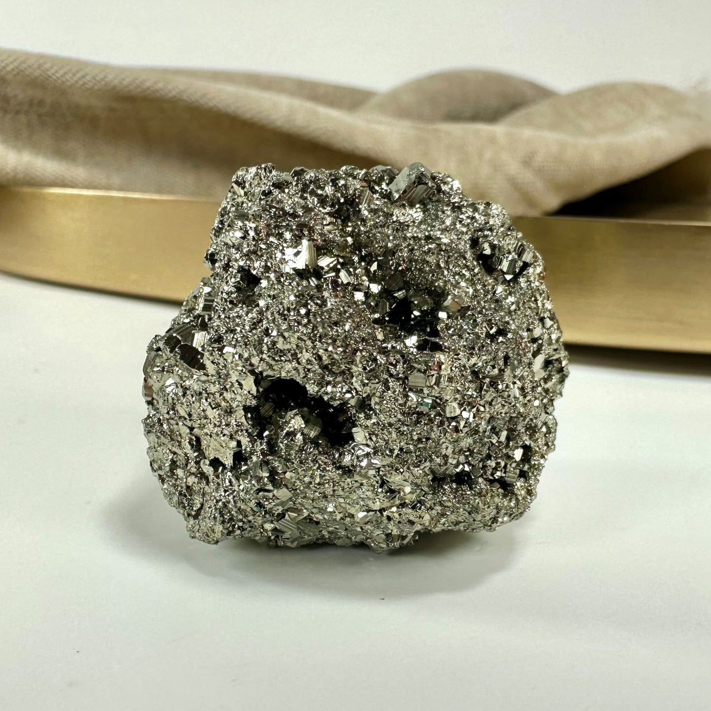 Rå pyrit sten på bord med lys baggrund og blødt tekstil i baggrunden.