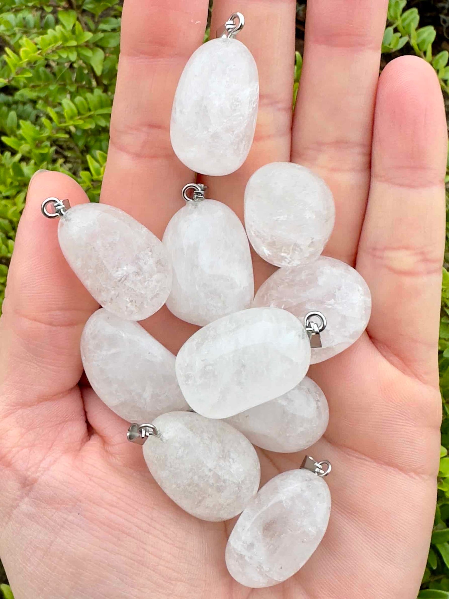 Hånd med flere glatte bjergkrystal vedhæng mod en grøn baggrund.