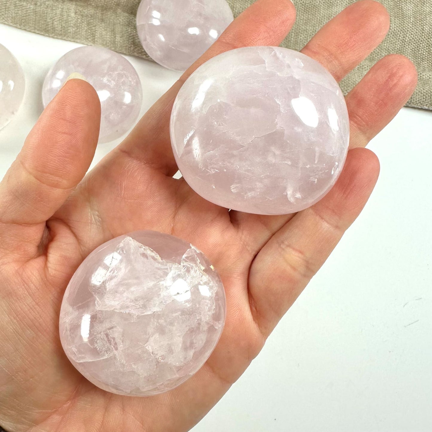 Hånd holder to glatte rosenkvarts palmstones. Flere sten ses i baggrunden.