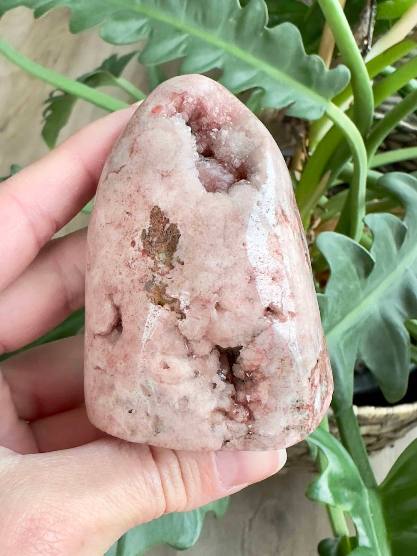 Lyserød ametyst i fri form holdt i hånden, omgivet af grønne planter.