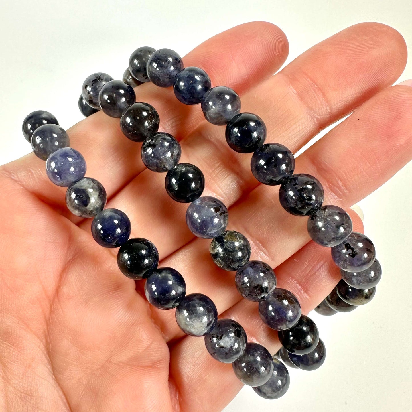 Hånden holder tre iolit armbånd lavet af polerede, mørkeblå perler.