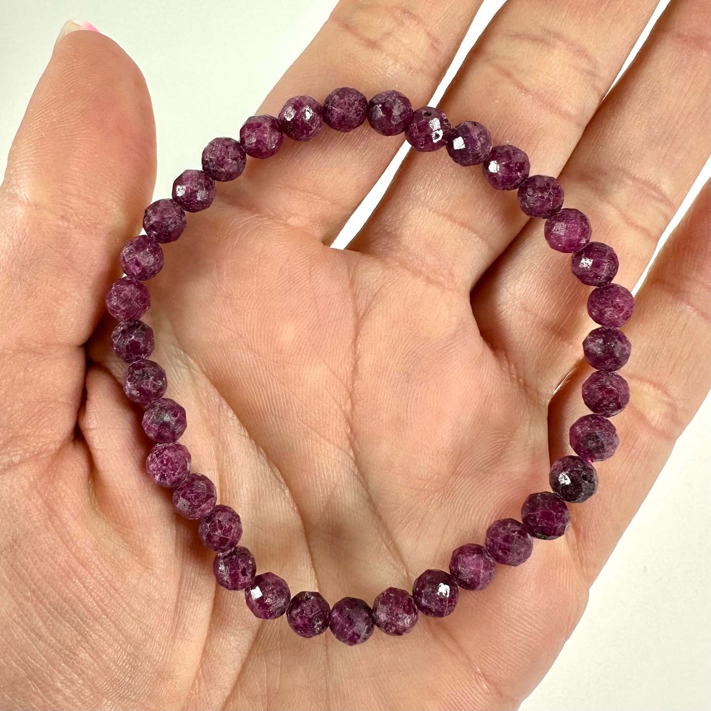 Rubin armbånd med facetterede perler, holdt i en hånd mod en lys baggrund.