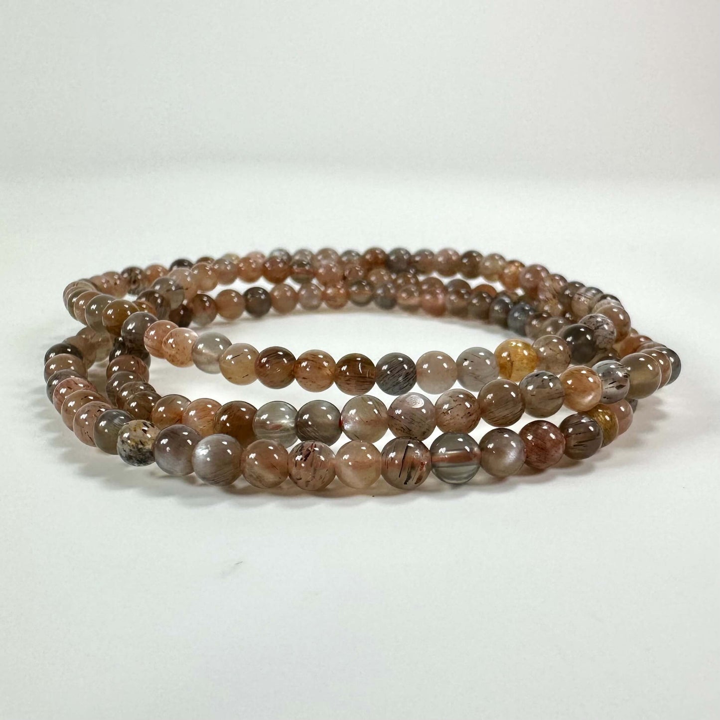 Et halskæde lavet af runde, flerfarvede stenperler i jordtoner, ligger fladt mod en hvid baggrund.