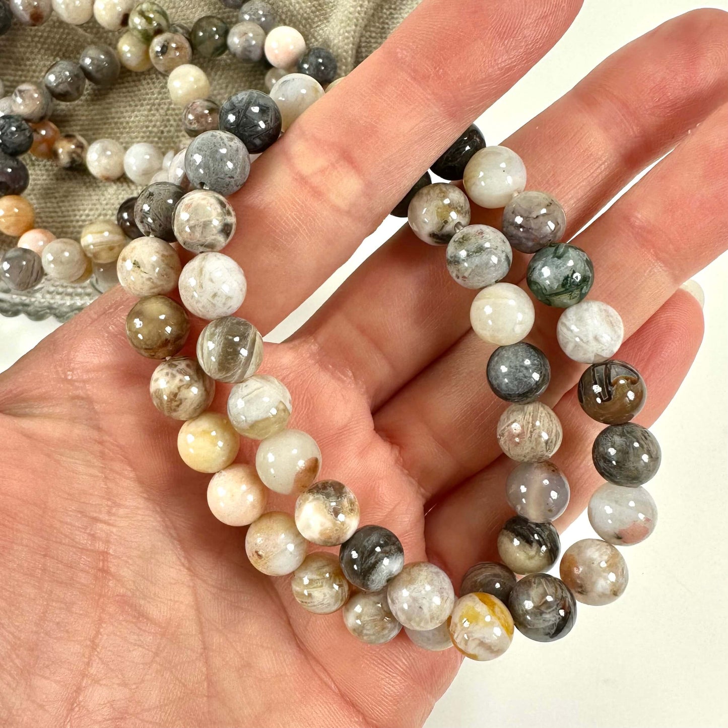 Hånd holder bambus agat armbånd med perler i forskellige nuancer på en lys baggrund.