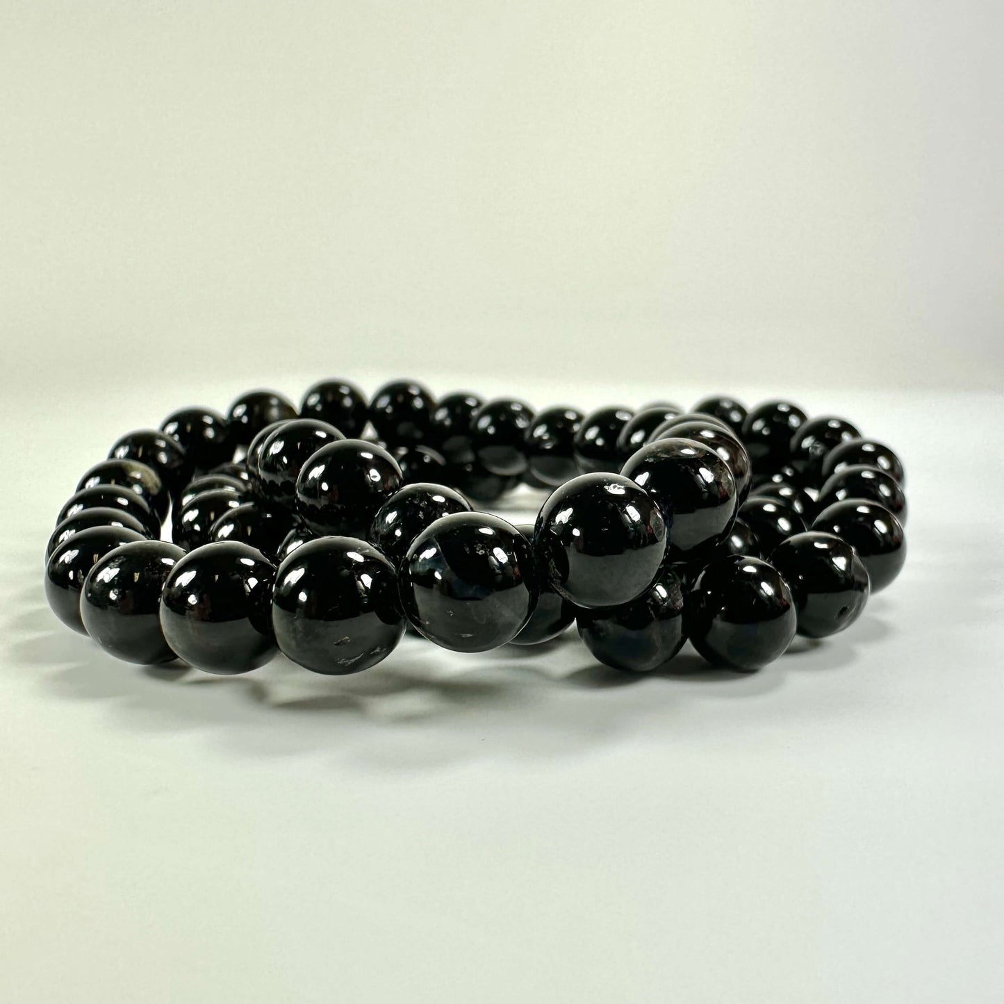 Sort armbånd af perler anbragt i en spiral på en hvid baggrund.