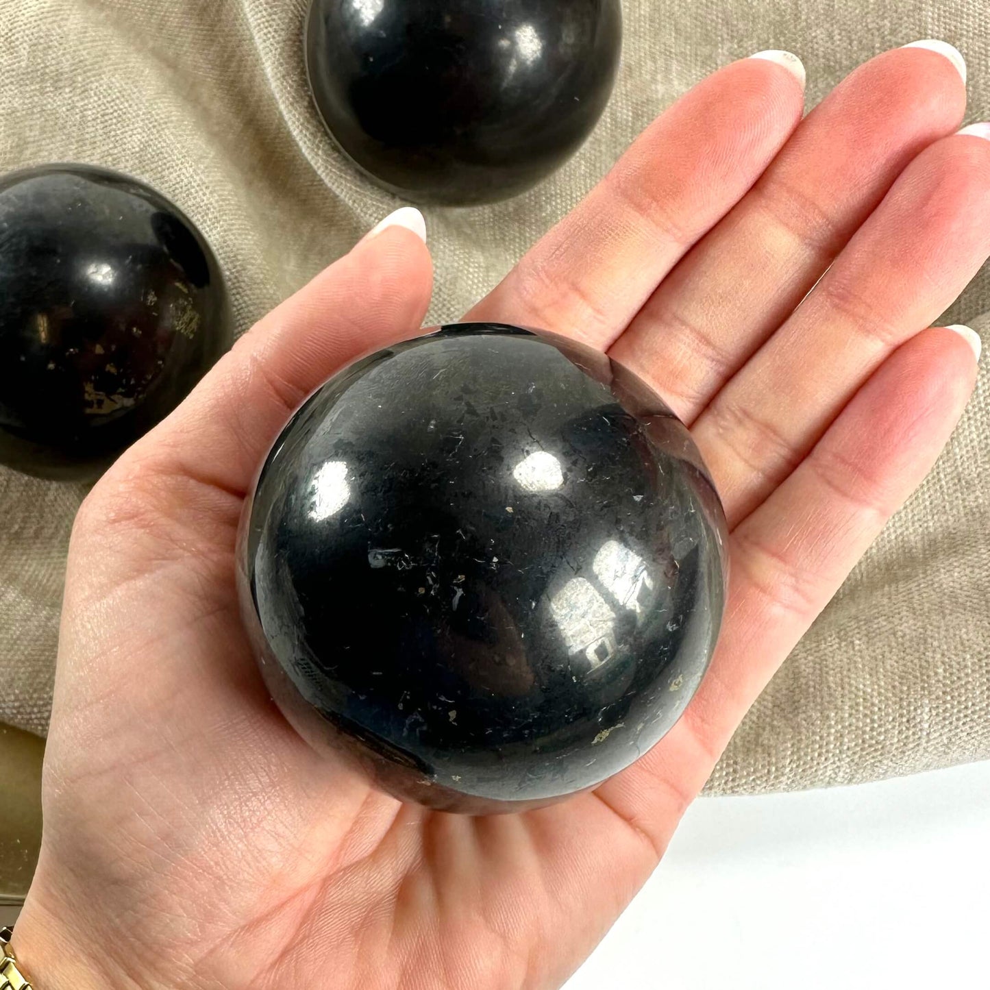 Hånd holder en skinnende shungit kugle med flere kugler i baggrunden.