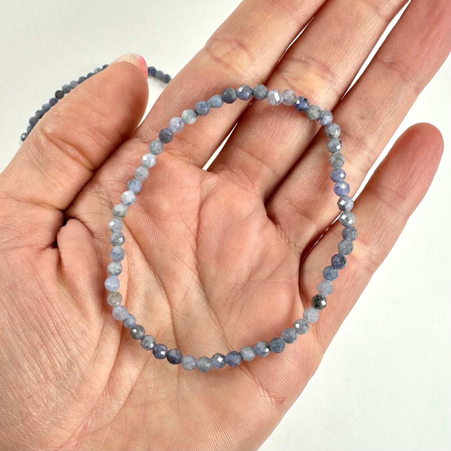 Hånd holder et tanzanit armbånd med små, facetterede blå sten mod en hvid baggrund.