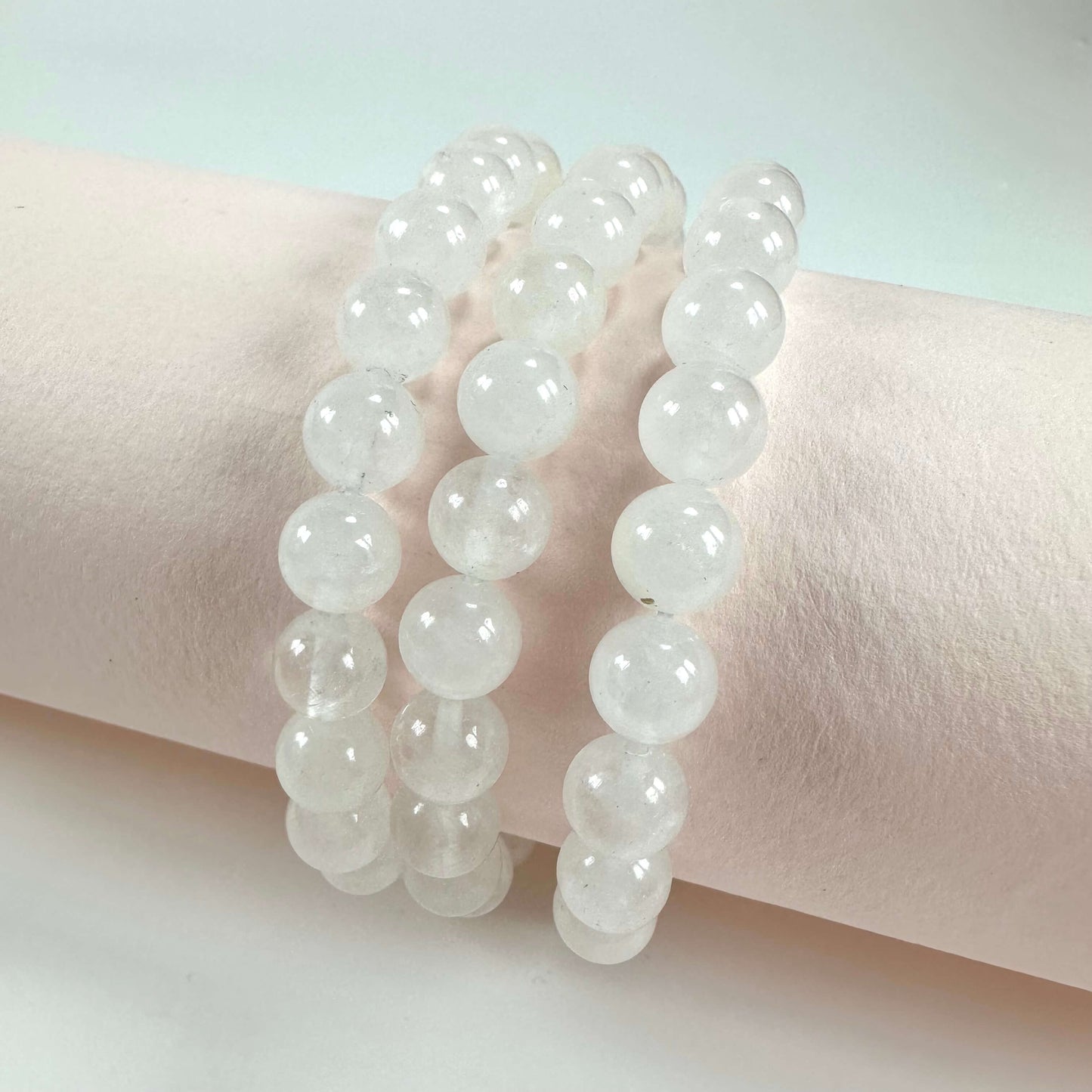 Tre rækker af bjergkrystal armbånd præsenteret på en cremefarvet baggrund.