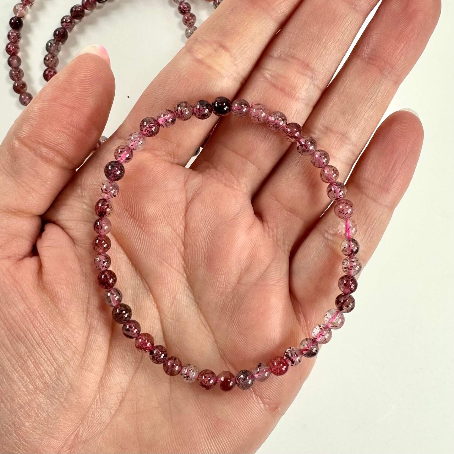 En hånd holder et Jordbærkvarts armbånd med små, runde, lyserøde perler.