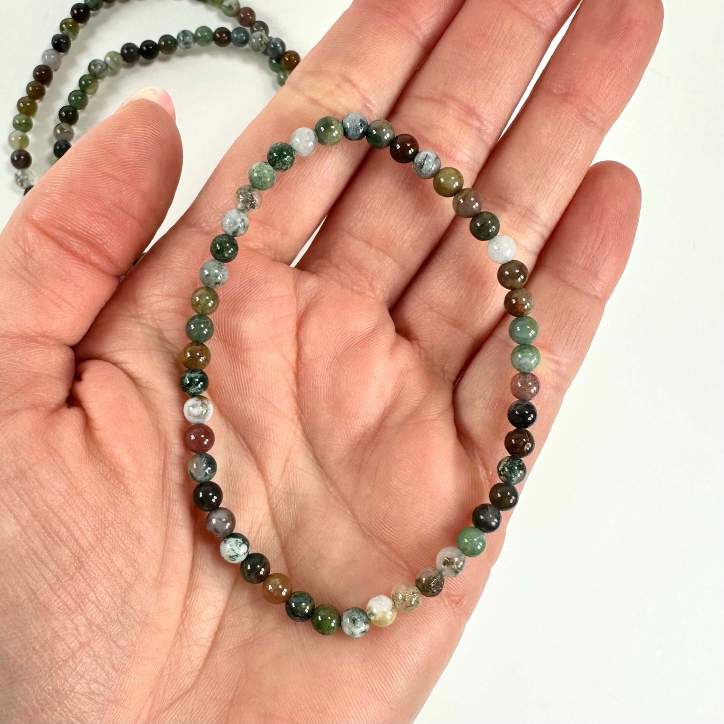 Hånd holder et indisk agat armbånd med runde, flerfarvede perler på en lys baggrund.