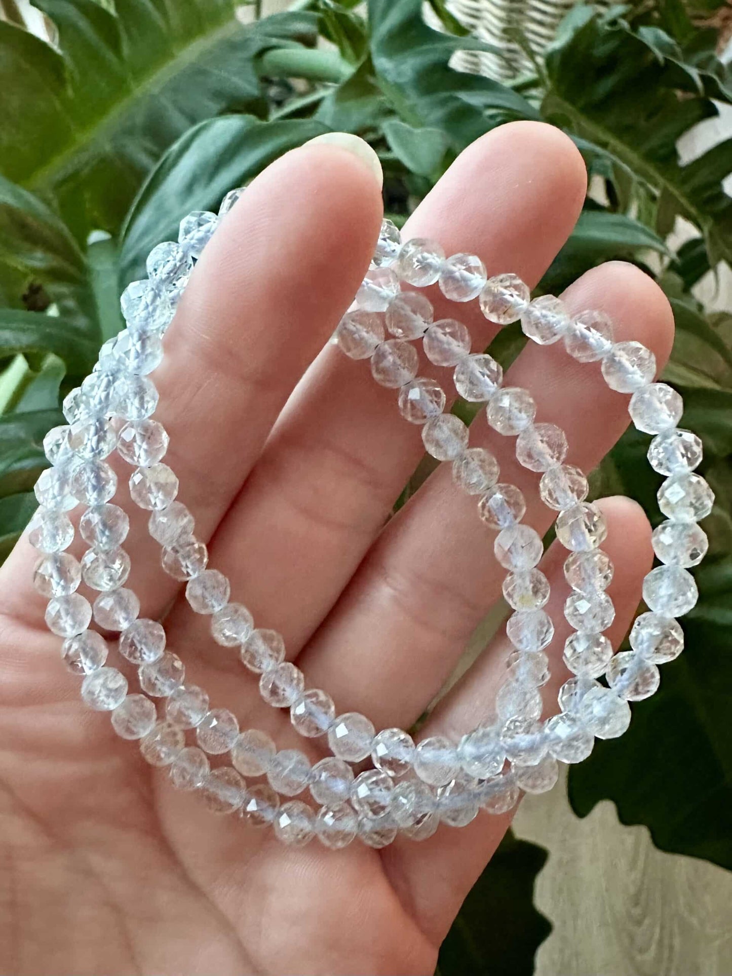 Hånd, der holder gennemsigtige Topaz armbånd foran grønne planter.