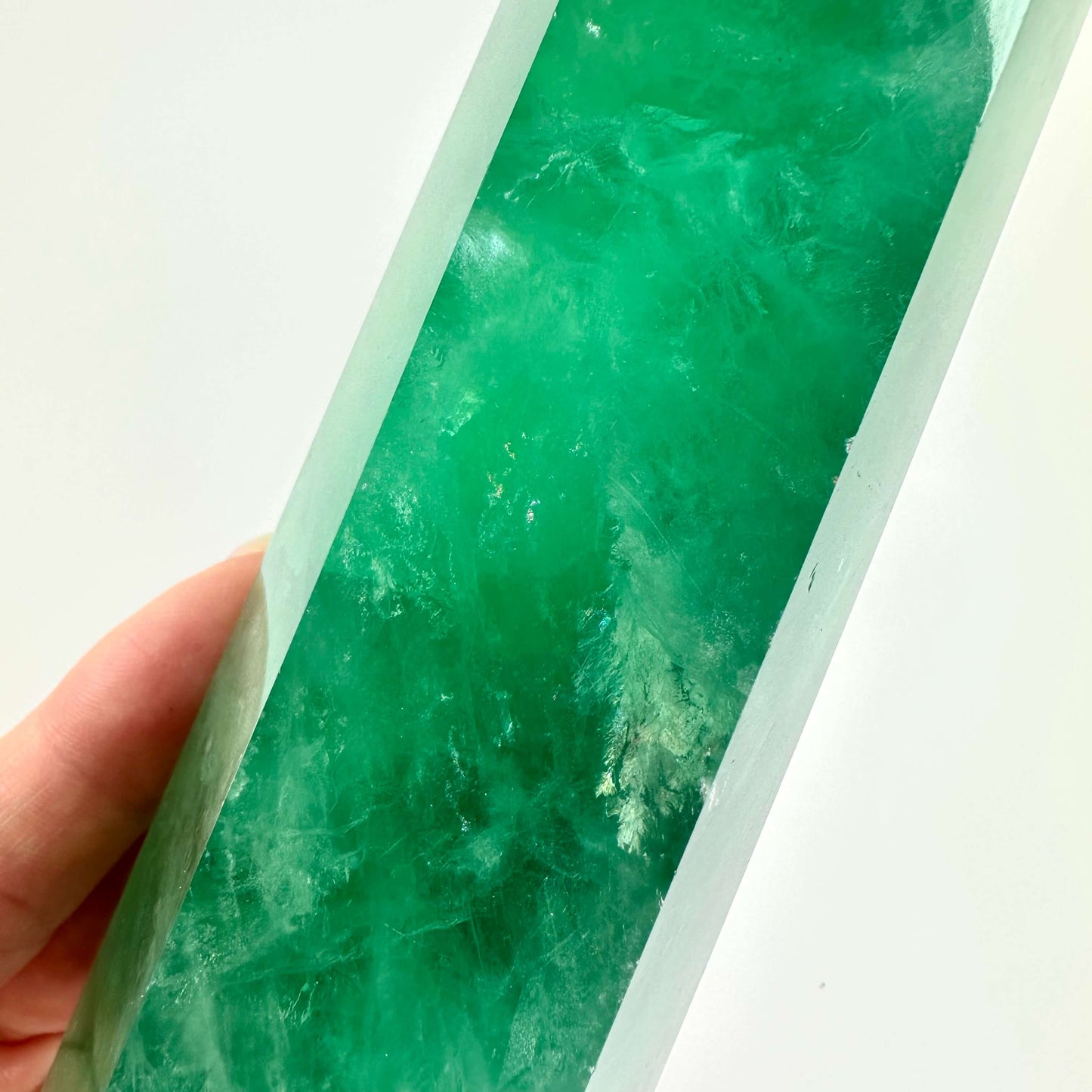 Hånd, der holder et grønt fluorit tårn mod hvid baggrund.