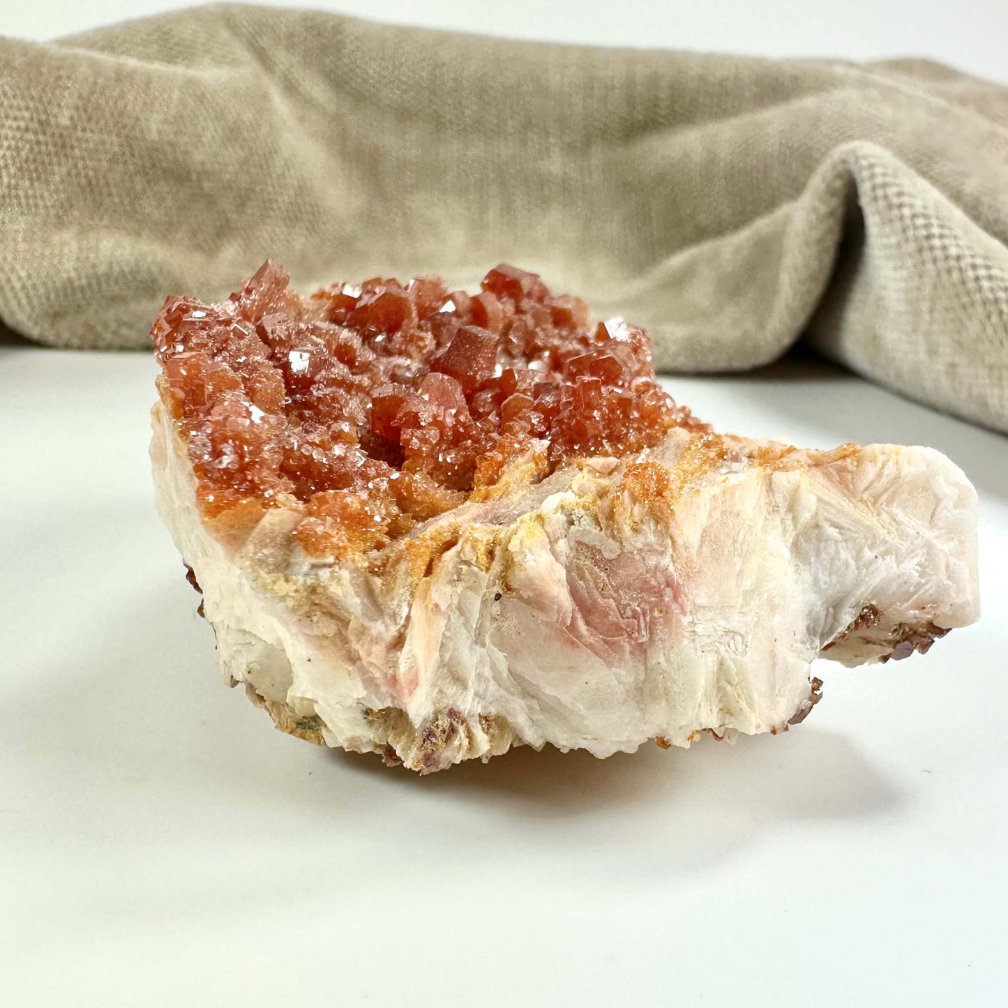 En klynge af røde krystaller på en lys klippe med en beige baggrund.