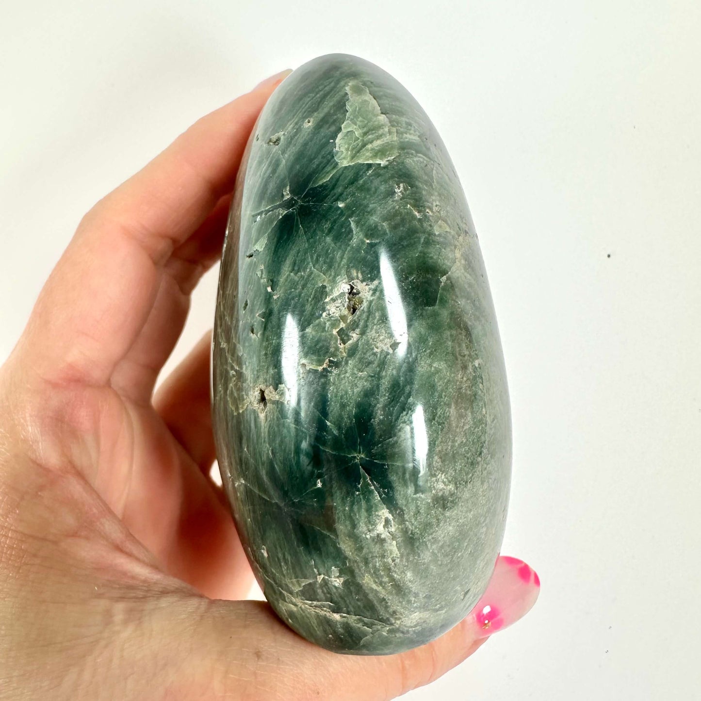 Hånd holder en poleret, grøn Jaspis hav sten i æggeform mod en lys baggrund.