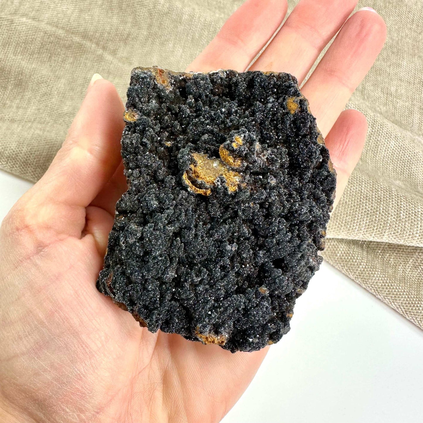 Hånd holder en mangan klynge med ru, krystallinsk tekstur og sorte farver.