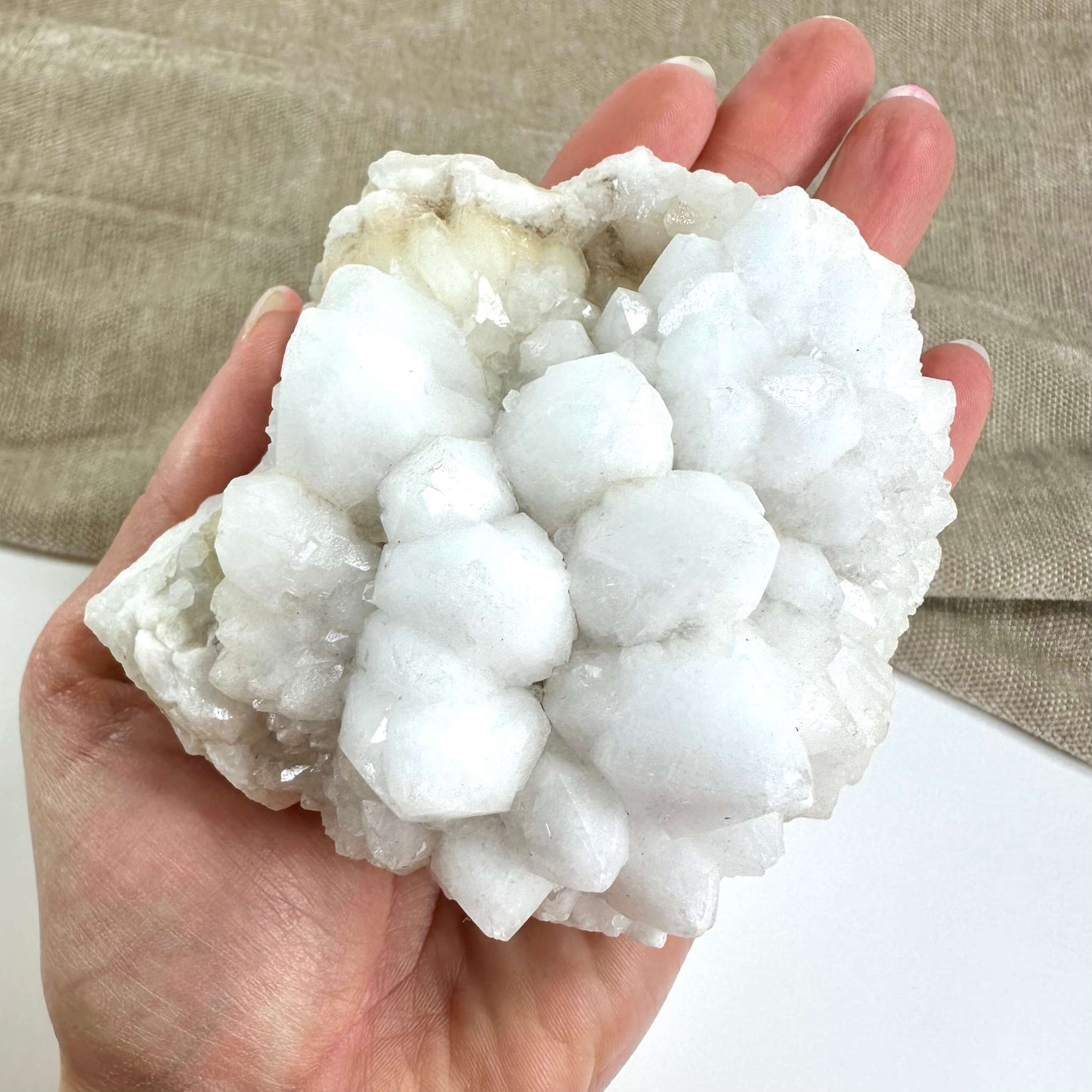 Hånd holder en blomster kvarts klynge mod en neutral baggrund.