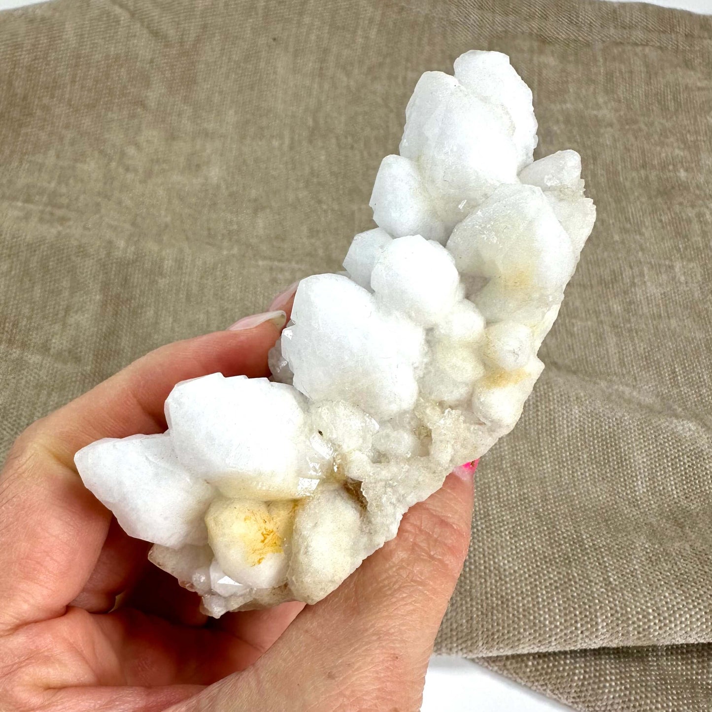 Hånd holder en blomster kvarts klynge med hvide og gyldne krystaller foran en brun baggrund.