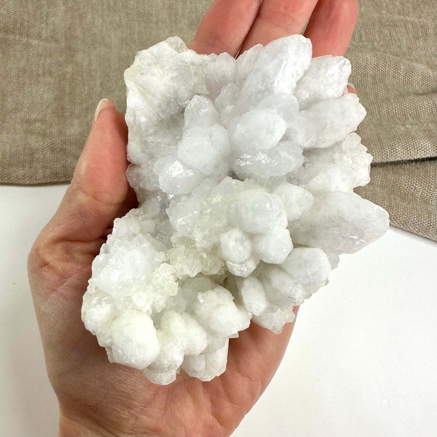 Hånd der holder en hvid Blomster kvarts klynge mod en beige baggrund.