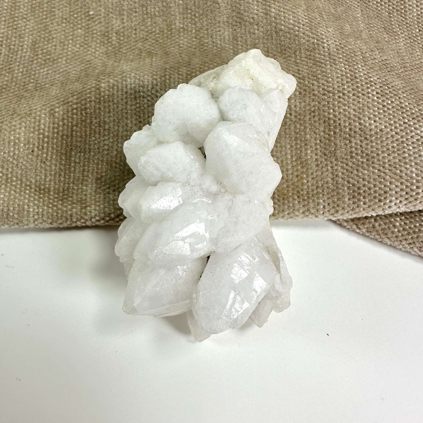 Blomster kvarts klynge med hvide, glinsende krystaller på en beige tekstilbaggrund.