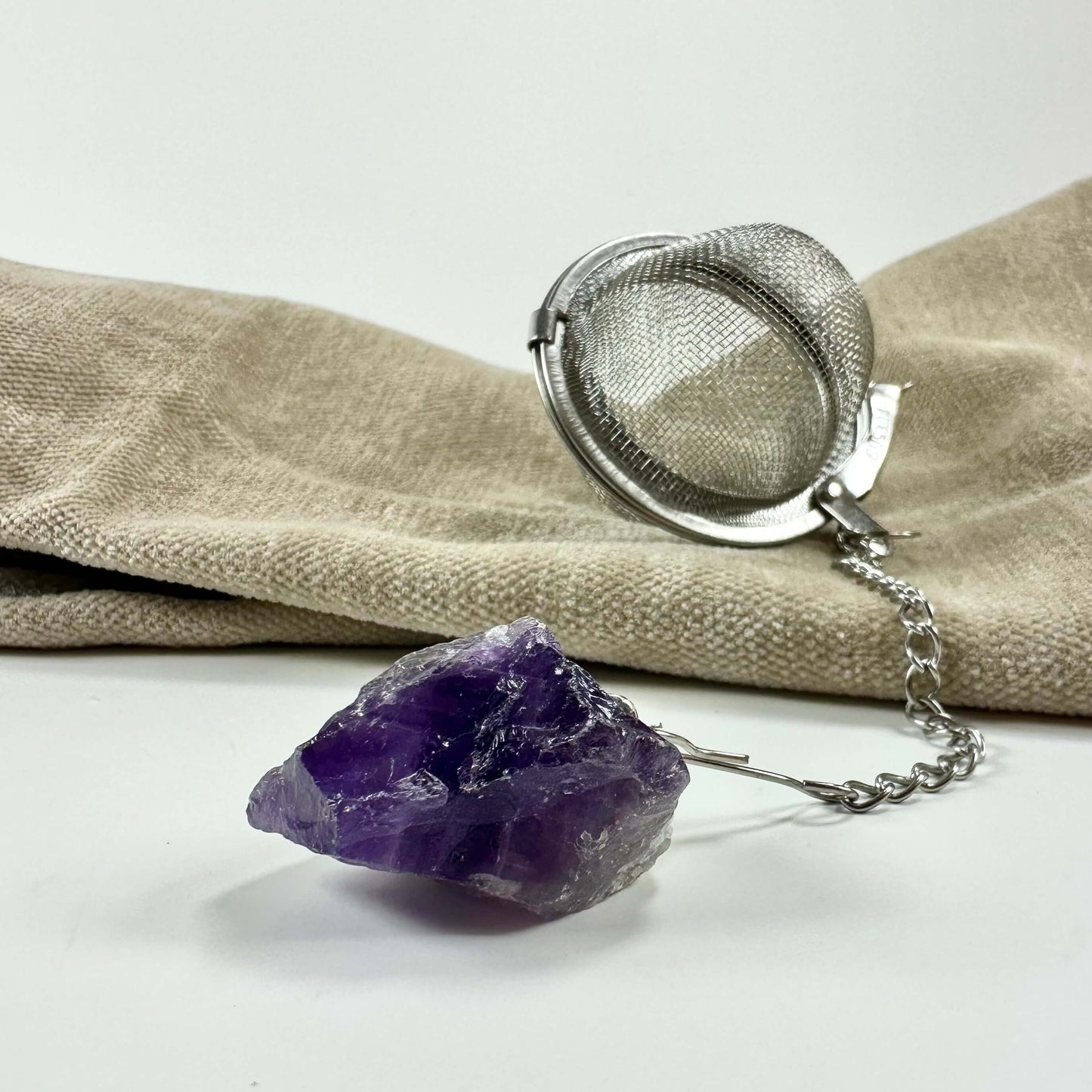 Te-infuser og ametystkrystal på beige klud.