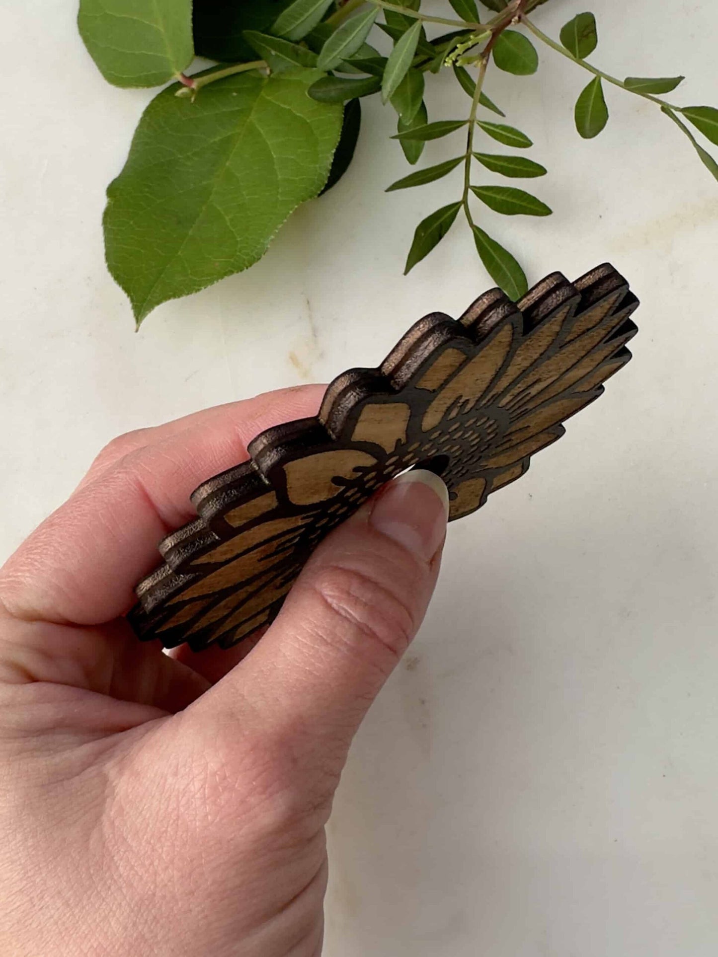 Hånd der holder en dekorativ kugle holder ved siden af grønne blade.