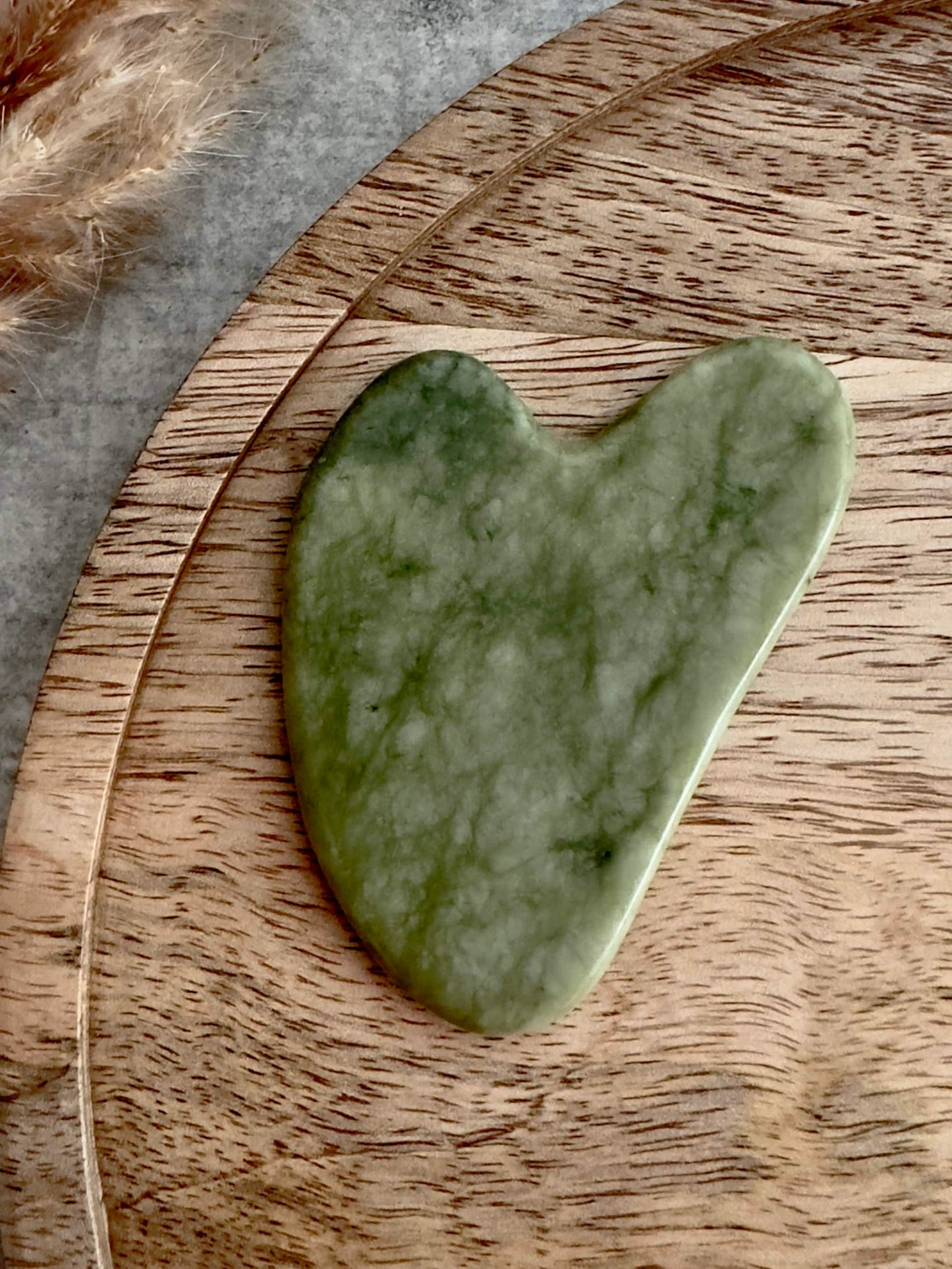 Gua Sha i grøn jade på en rund træbakke, klar til ansigtsmassage og skønhedspleje.