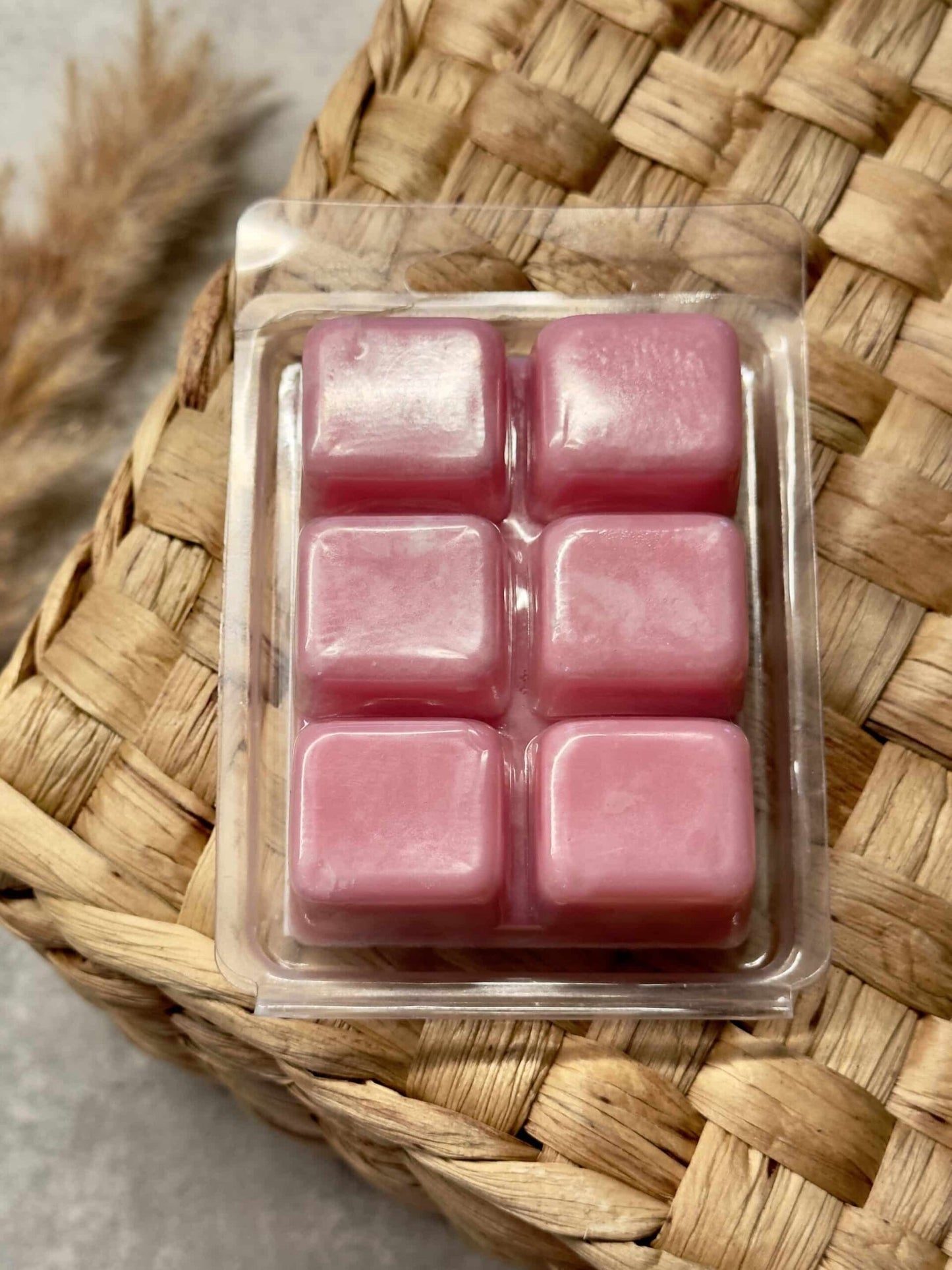 Pakke med rosa soyavokskuber, Pina Colada duft, på en flettet kurv baggrund.