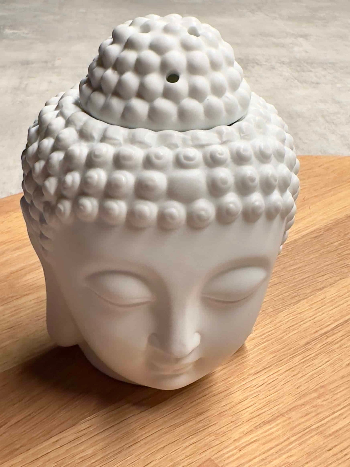 Voksbrænder med Buddha-hoved i hvid keramik på træbord, brugt til aromaterapi.