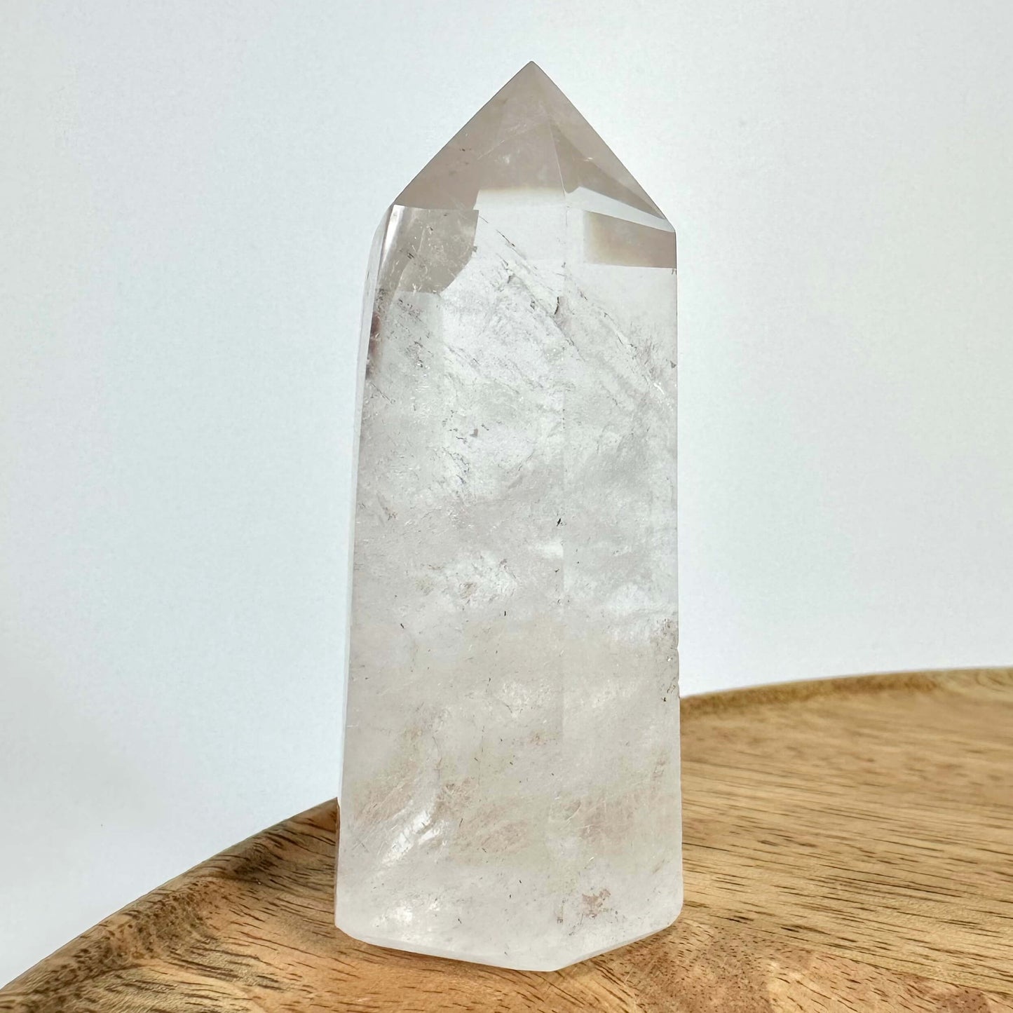 Klar bjergkrystal tårn på en træoverflade mod en hvid baggrund.