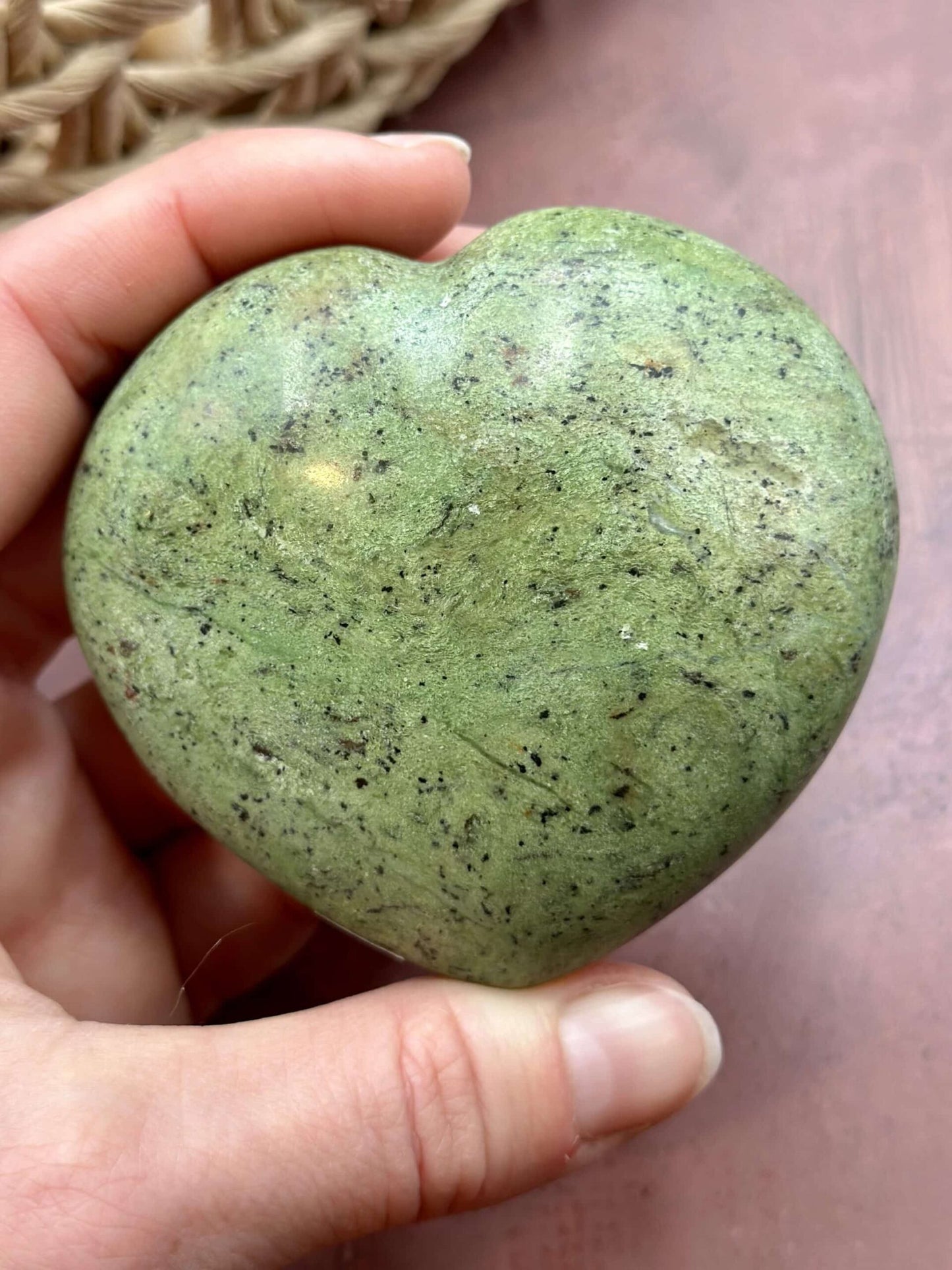 Hånd holder et hjerteformet chrysopras, grøn med naturlige mønstre. Baggrund i brunlige nuancer.