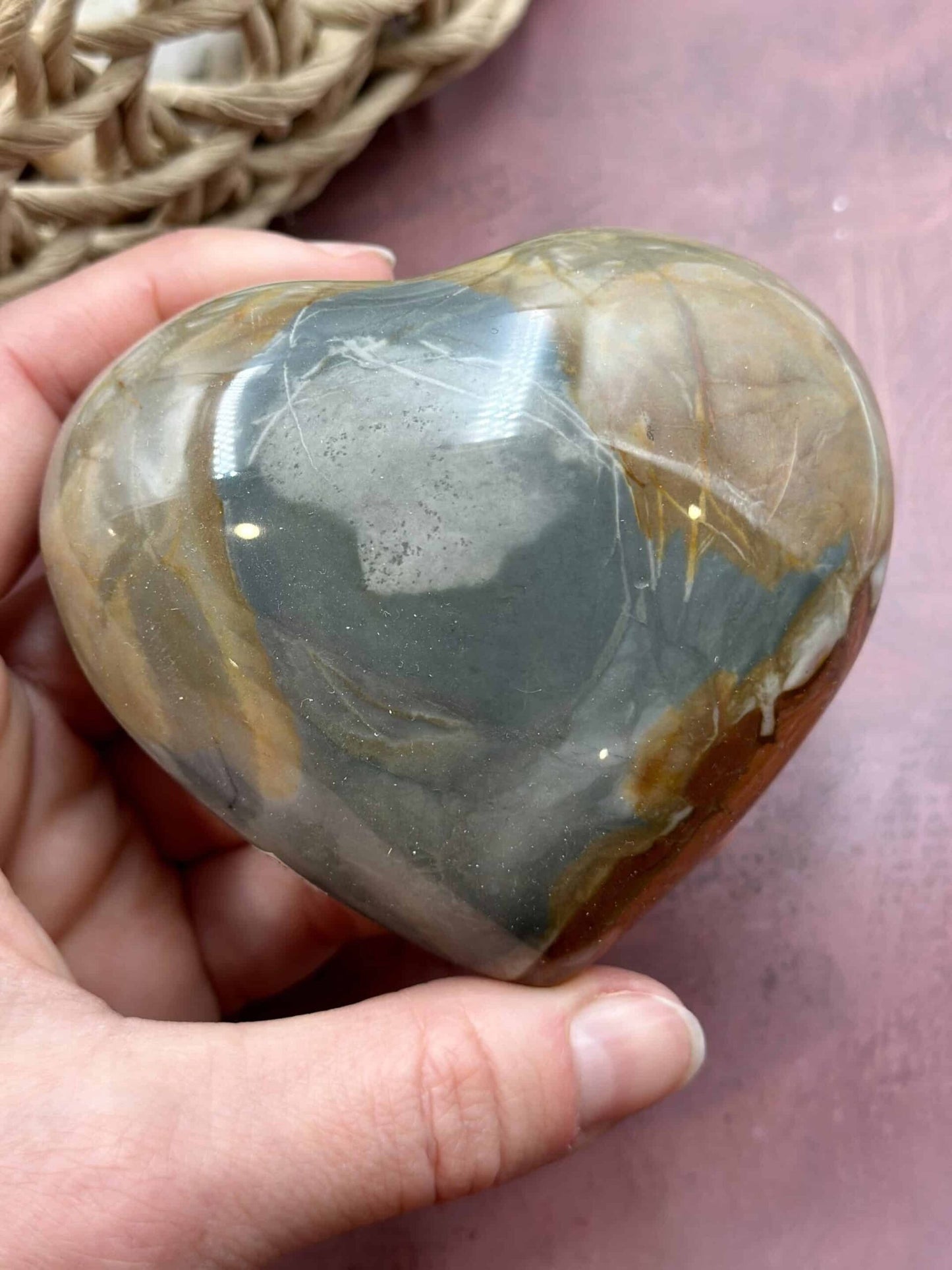 En hånd holder et Jaspis Polychrome hjerte med naturlige farvenuancer, på en lyserød baggrund.