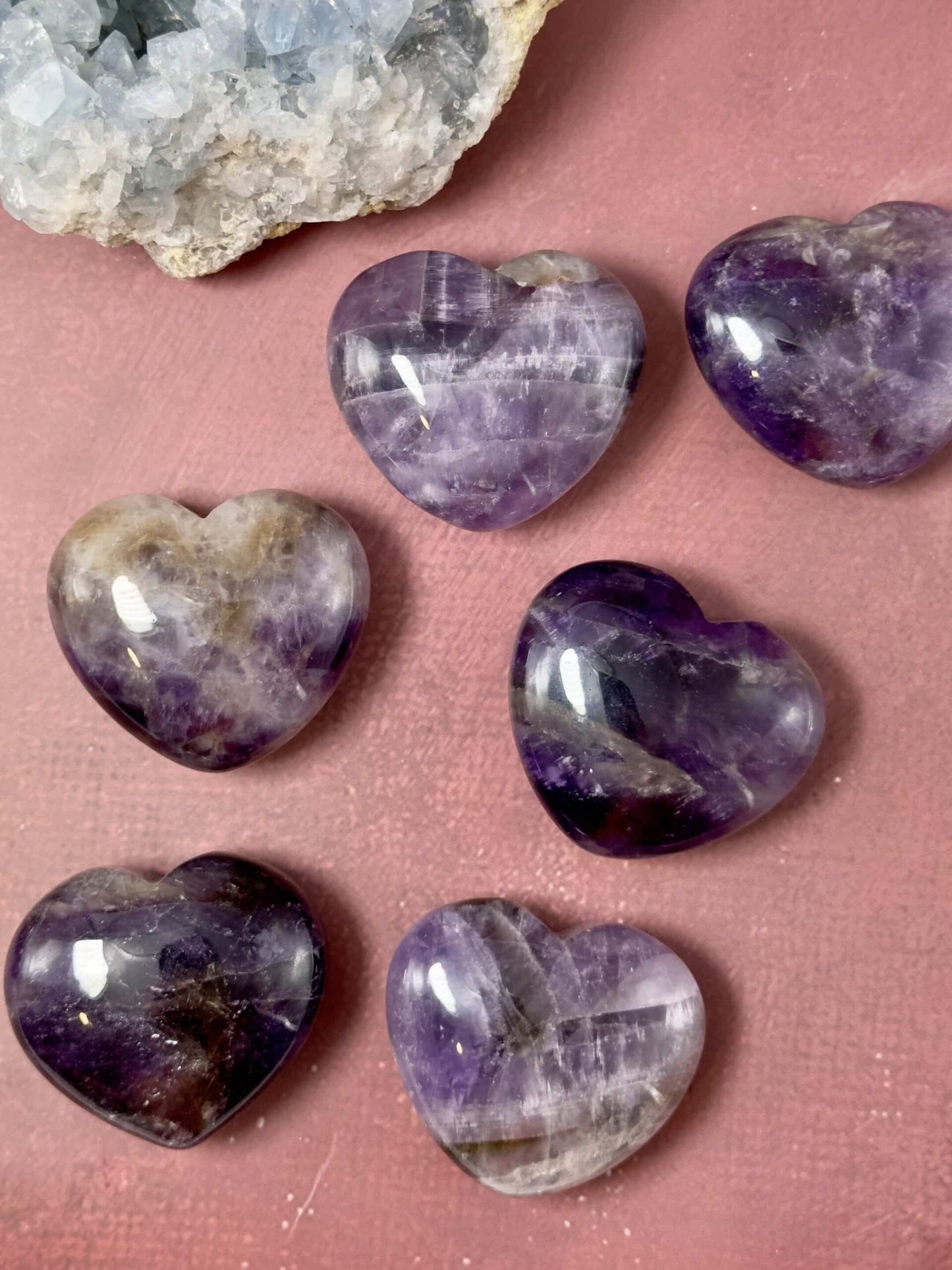 Ametyst hjerter på en rosa overflade ved siden af en stor krystal.